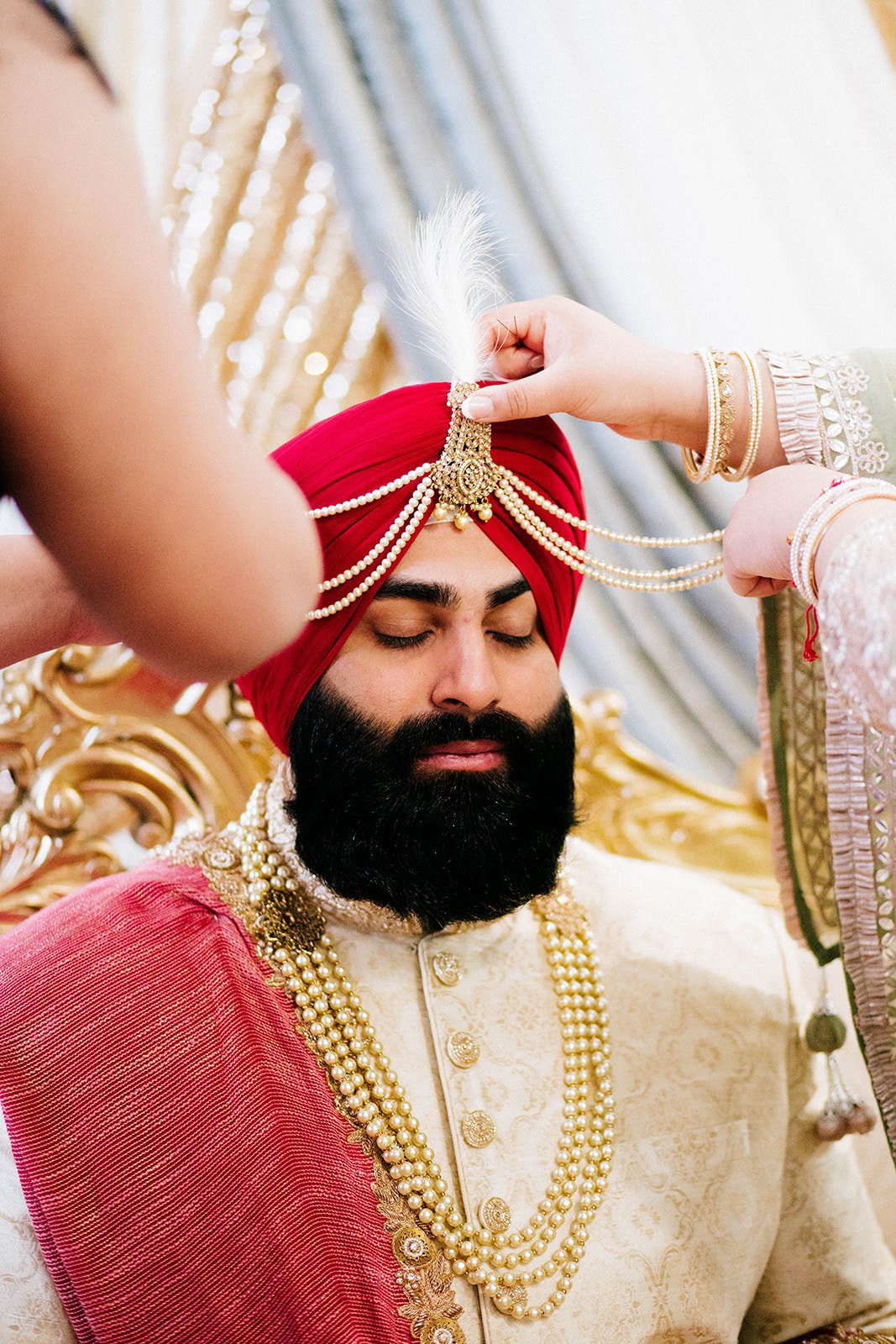 A groom has a traditional ornate kalgi placed onto his red turban. 