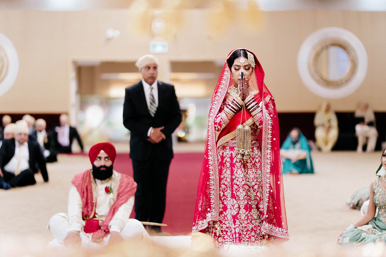 A indian bride in traditional dress is escorted by his parents down the aisle in a gurdwara