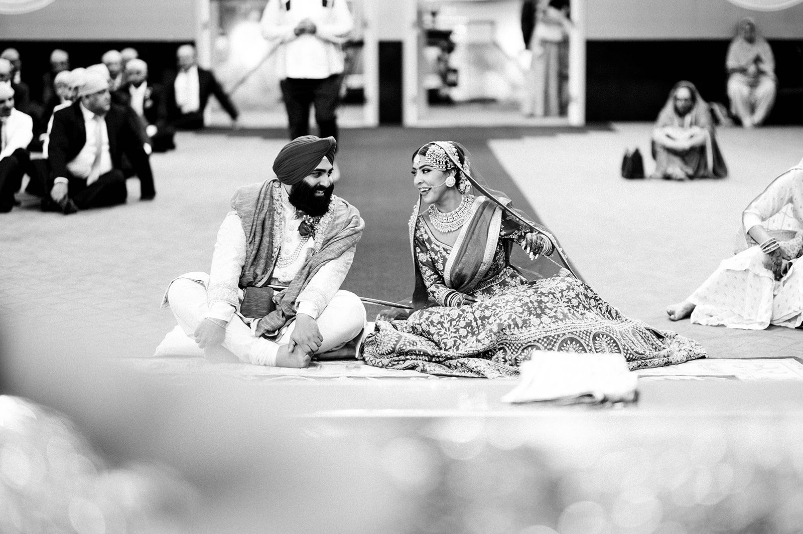 An indian bride and groom have a quick chat after the bride joins the groom sitting at the end of the aisle. 