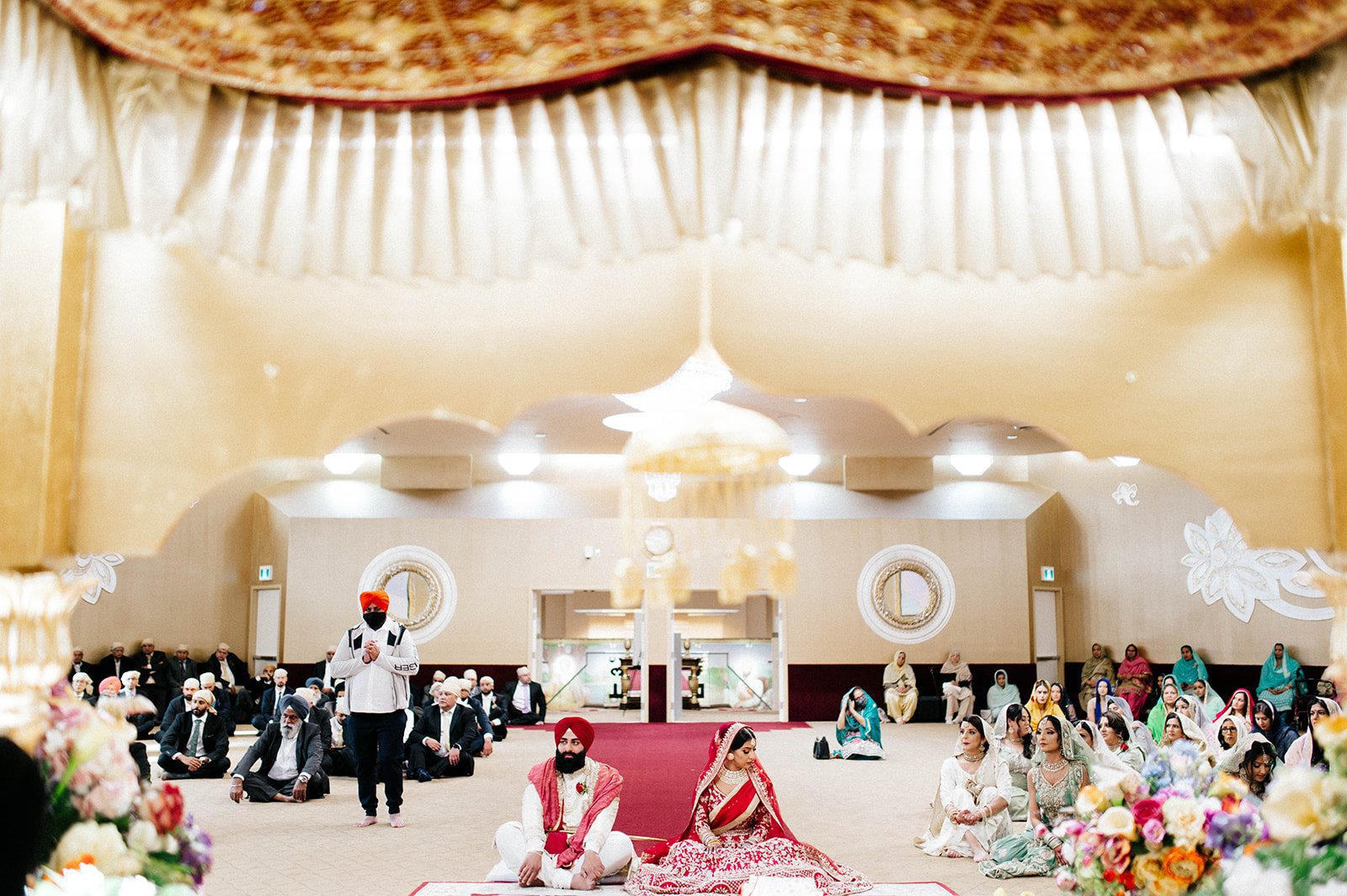A traditional Indian bride and groom are framed by curtains in a gurdwara. 