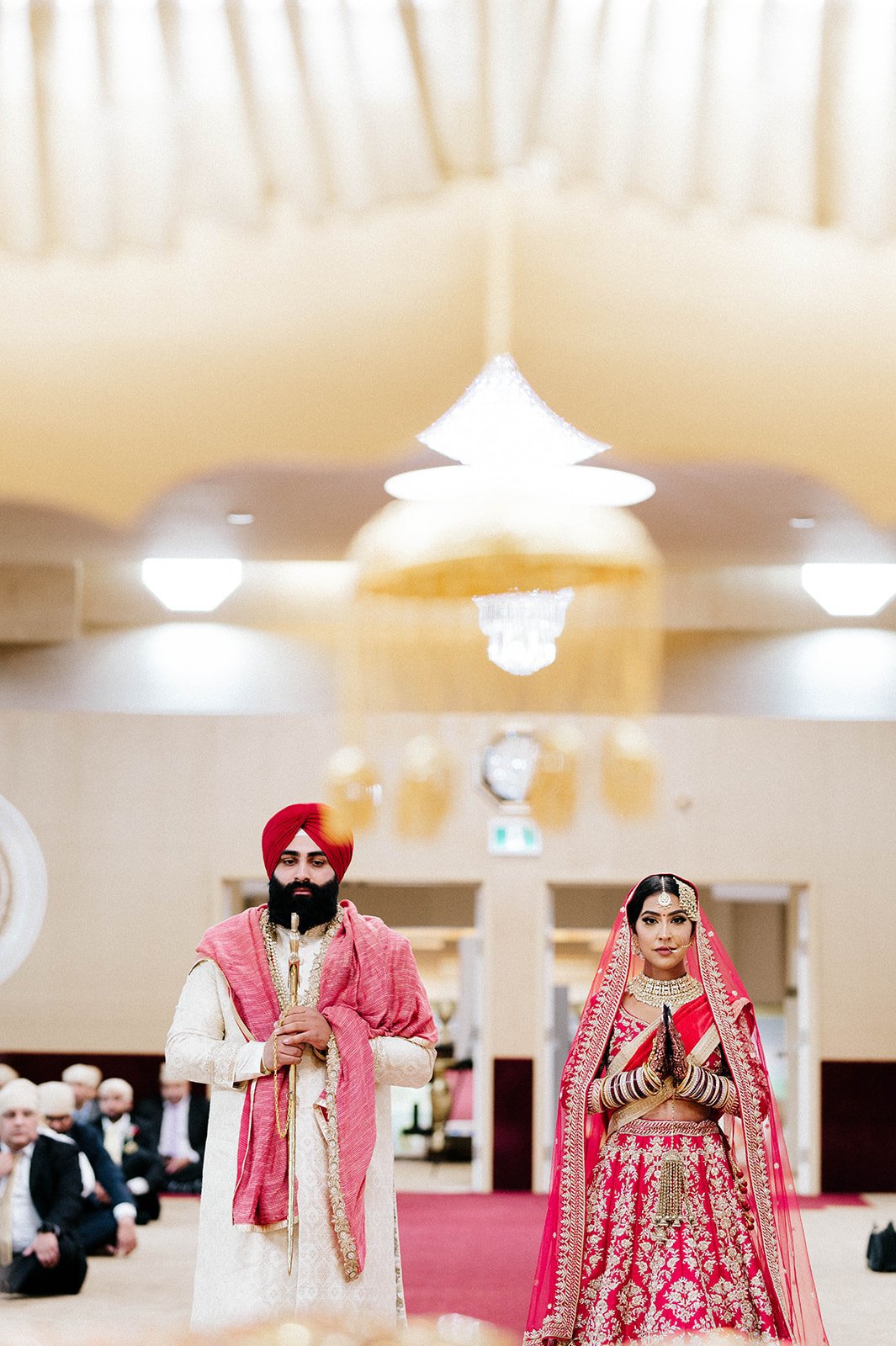 A bride and groom, both dressed in red, stand to pray.