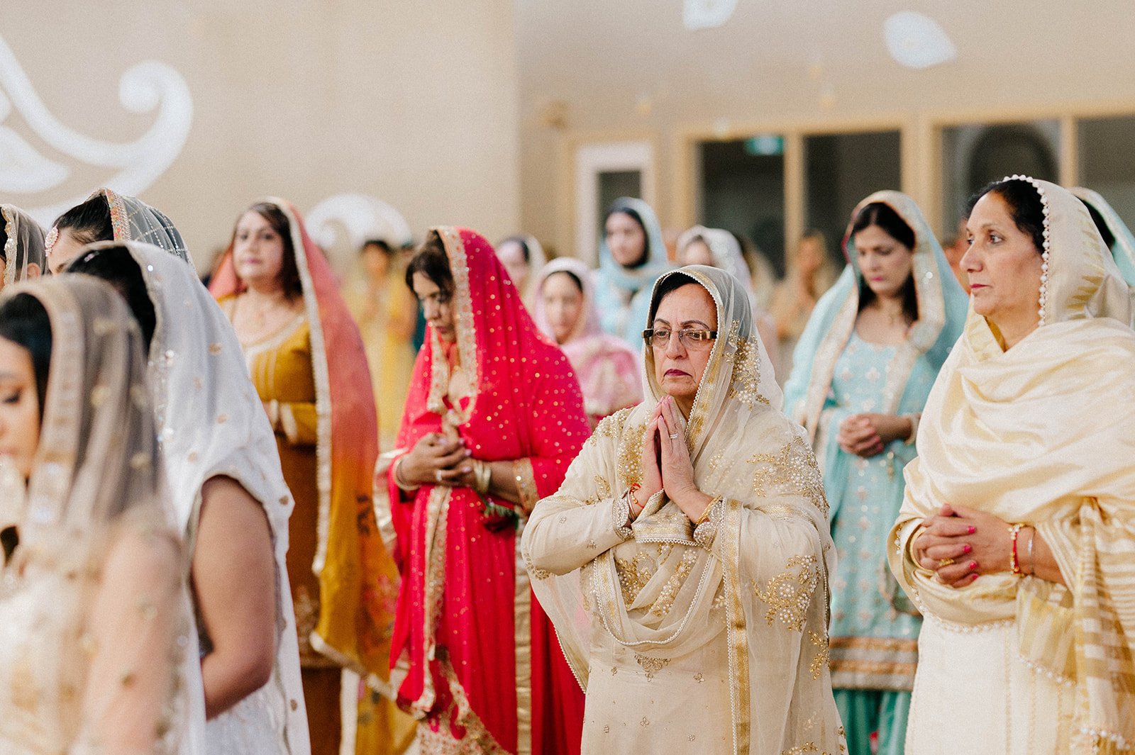 Women in colourful indian outfits stand to pray in a traditional indian ceremony. 