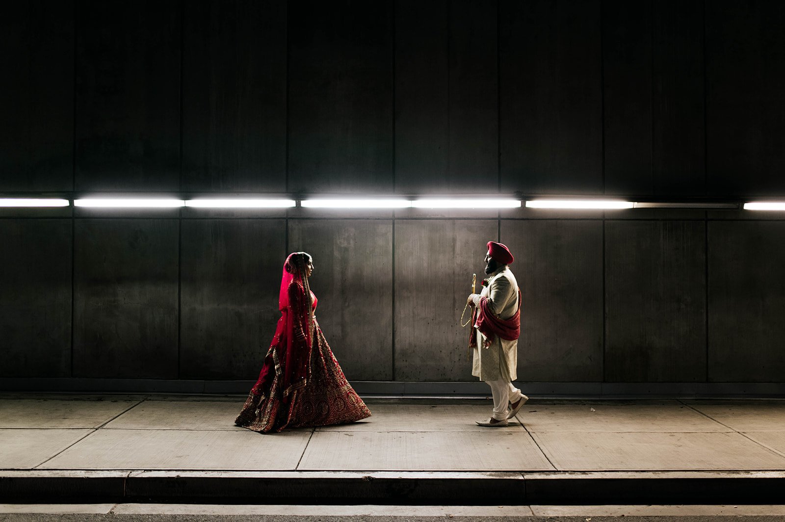 An Indian couple walk towards each other in a cinematic backlit photo in a tunnel under vancouver, BC.  
