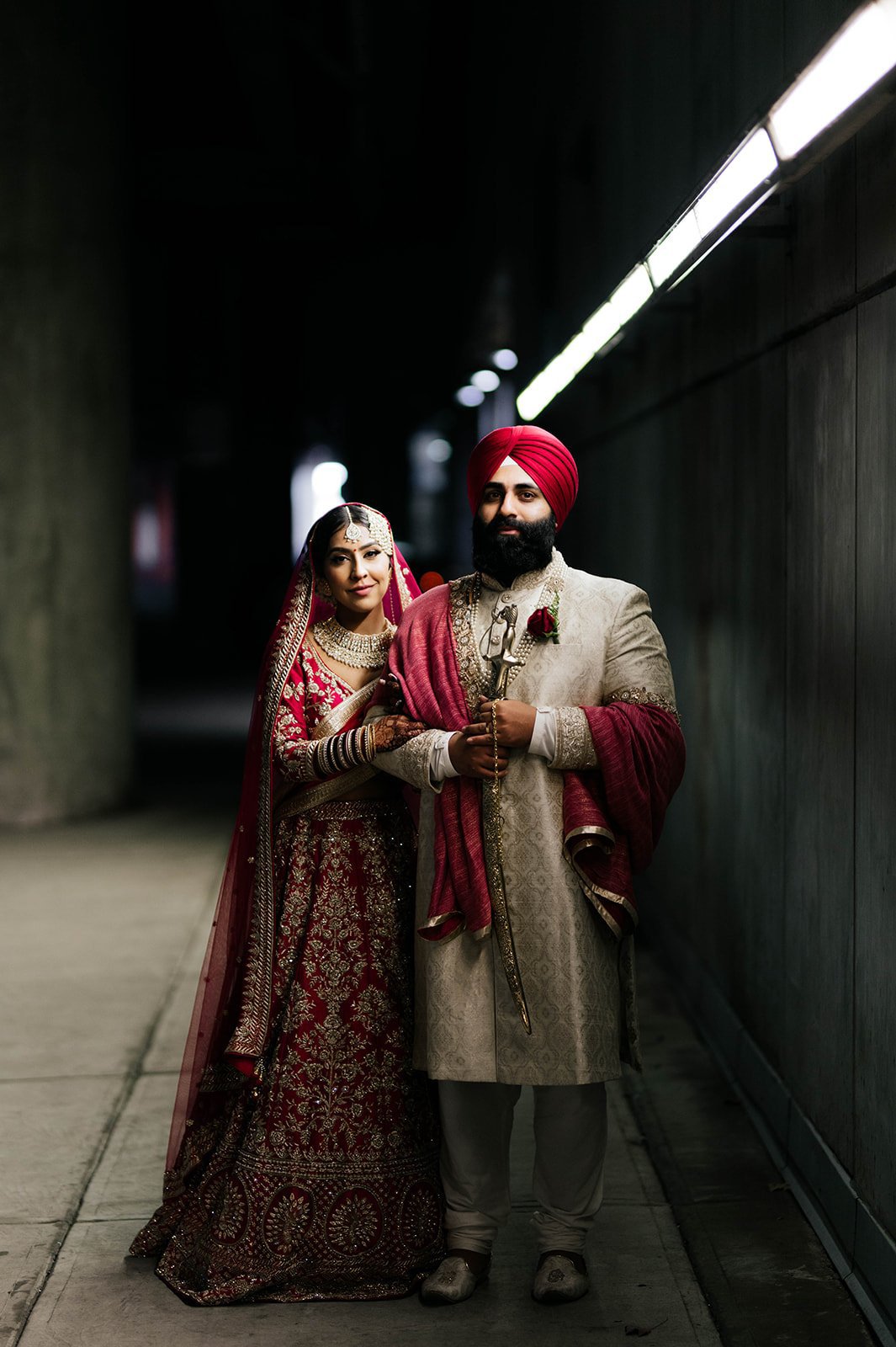 An Indian couple in traditional wedding attire embrace in a cinematic backlit photo in a tunnel under vancouver, BC. 