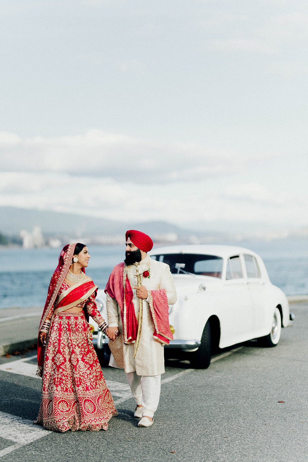 An indian couple struts away from a white vintage car along the seawall in Vancouver BC 