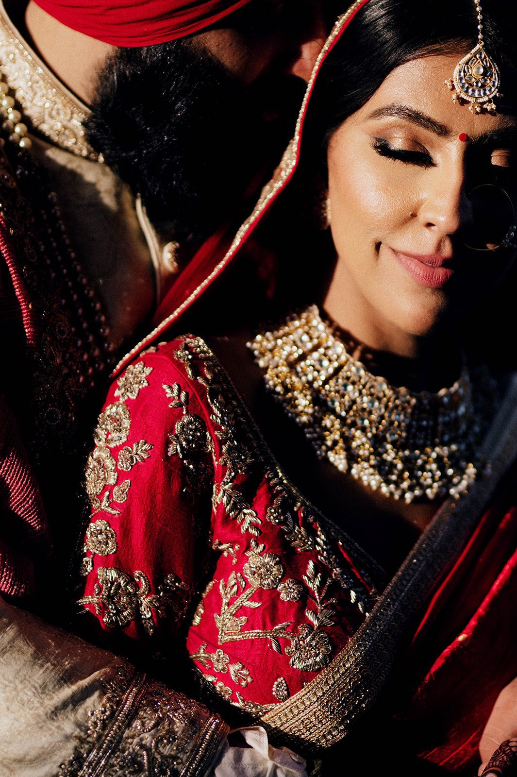 An Indian groom cuddles into his bride in close up photograph.