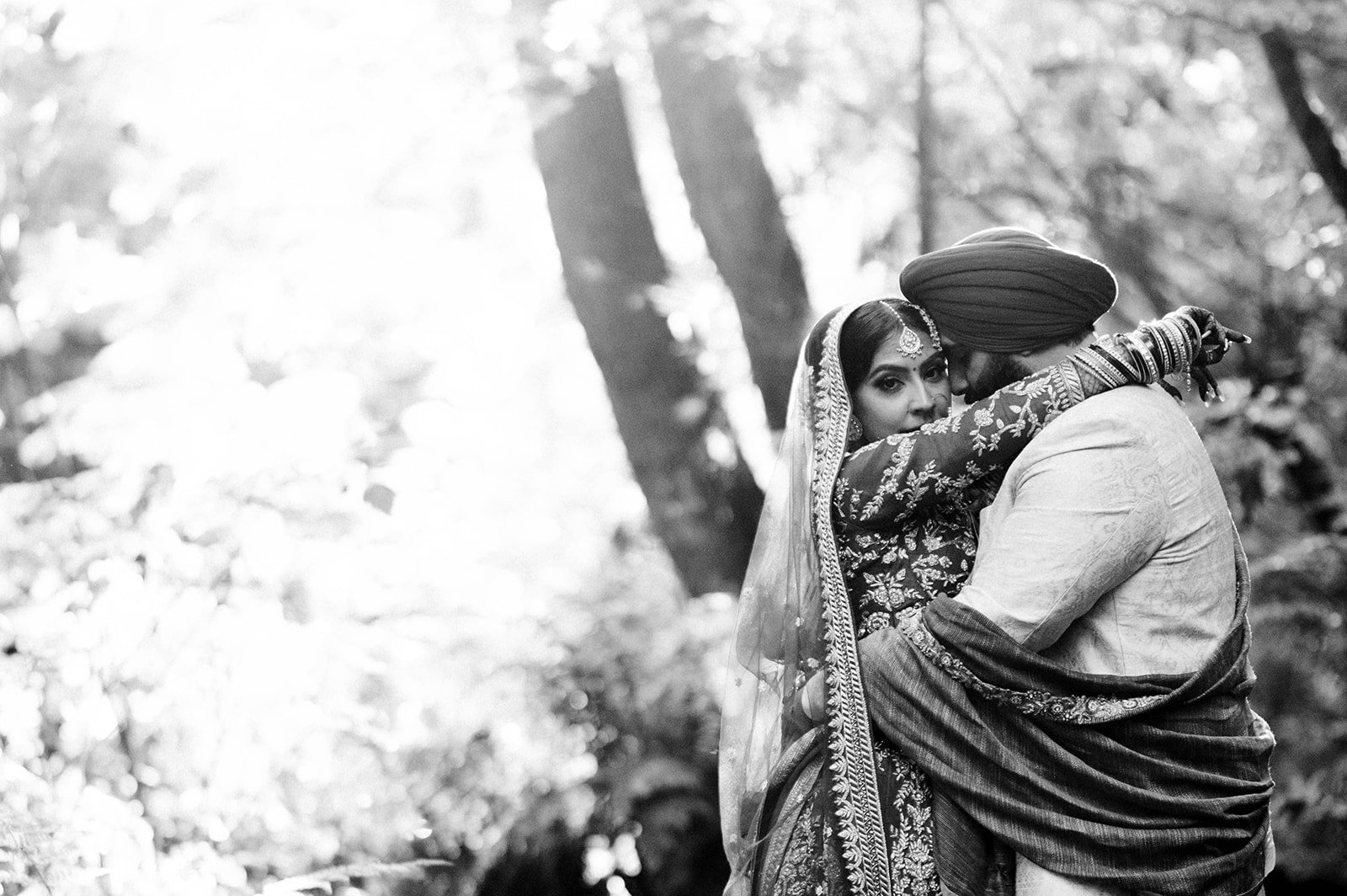 an indian couple cuddles in front of trees and leaves as the sunsets cinematically. 