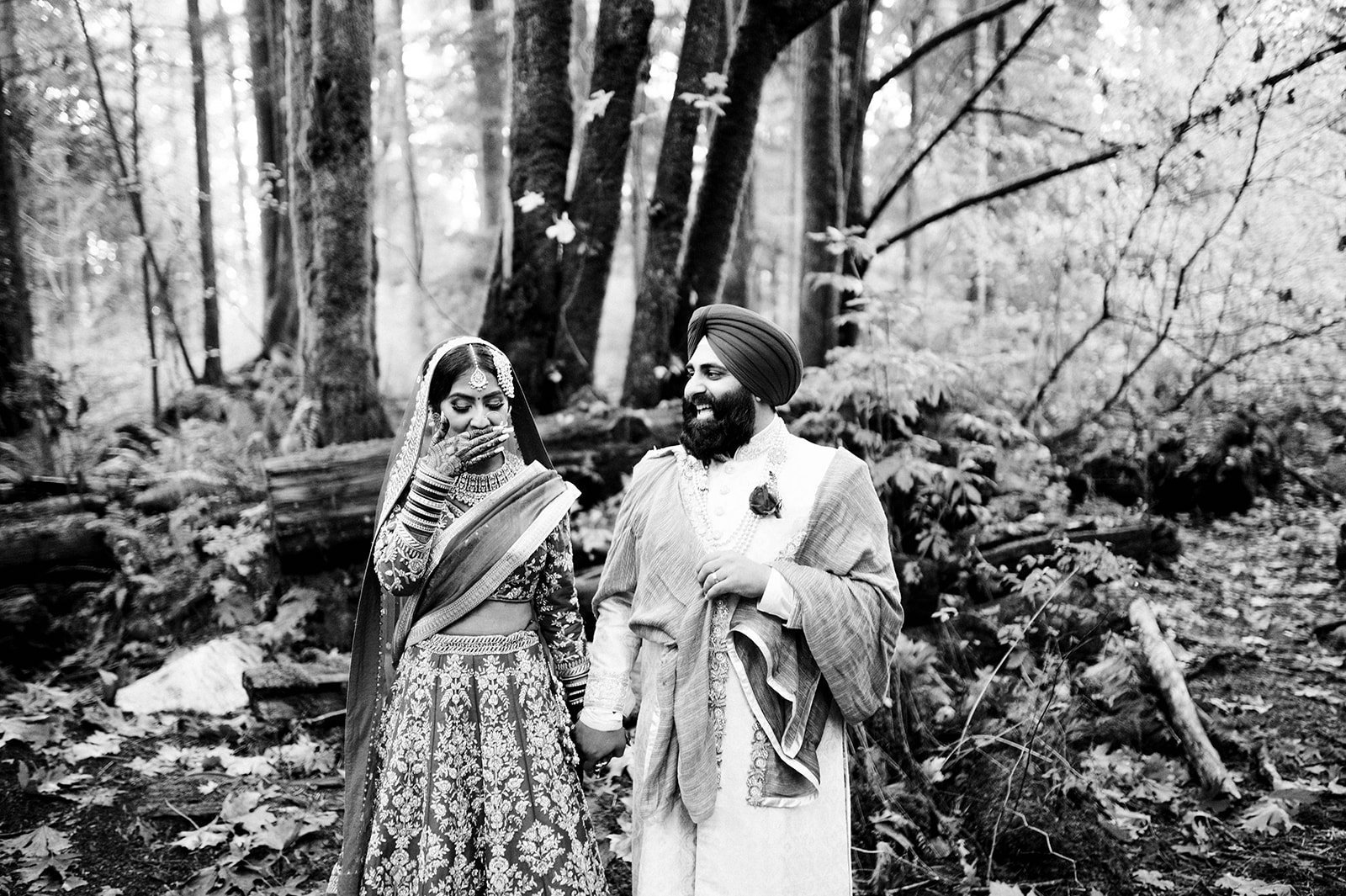 A south Asian bride laughs at her groom as they stroll through the forest in Stanley Park