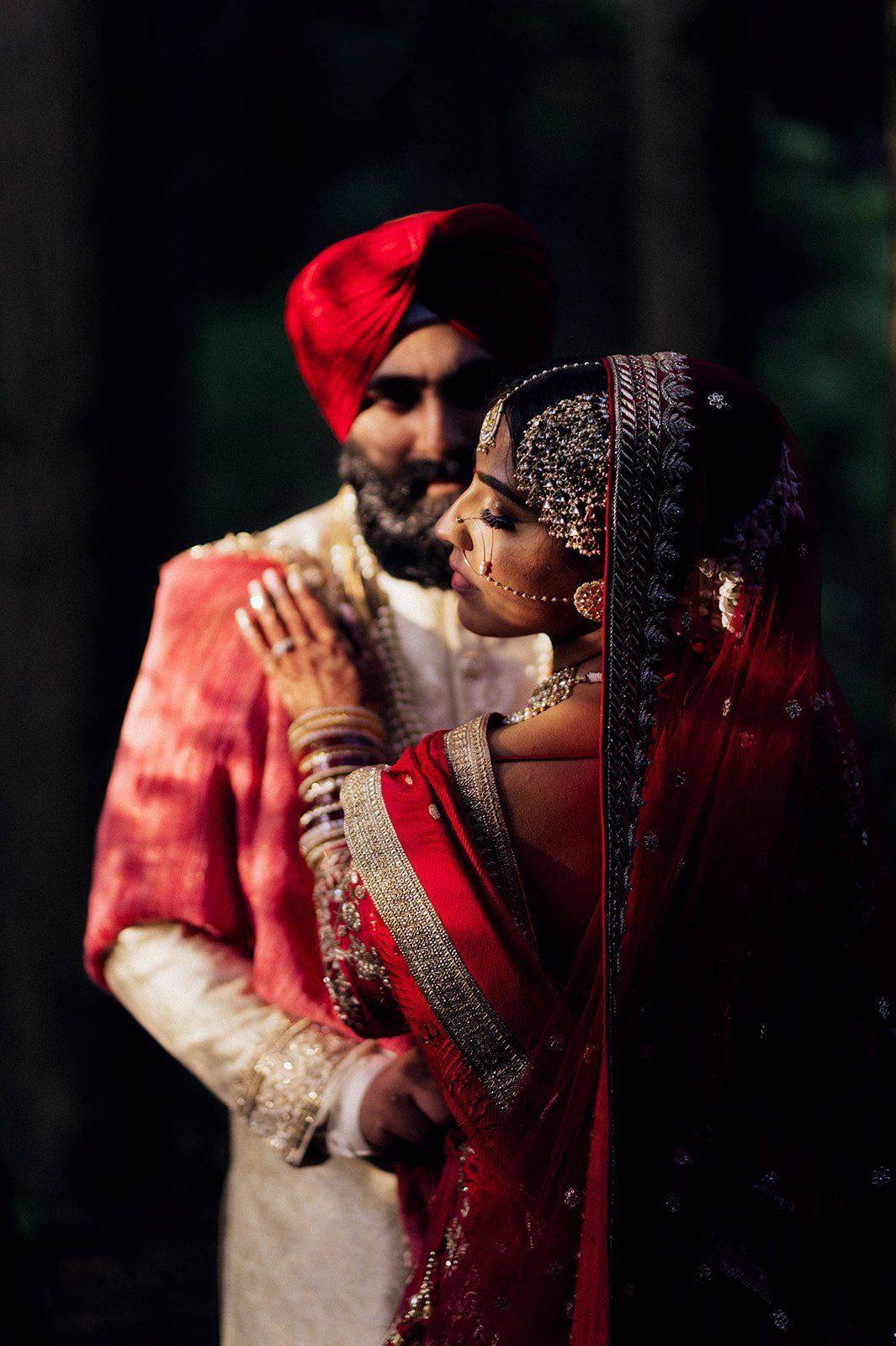 A south Asian groom holds his bride and she looks away, wreathed in shadow and harsh light in Vancouver BC. 