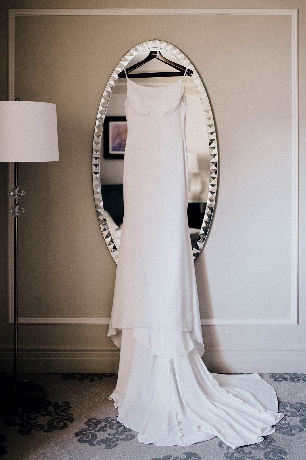 An elegant white wedding dress hangs from a round mirror.