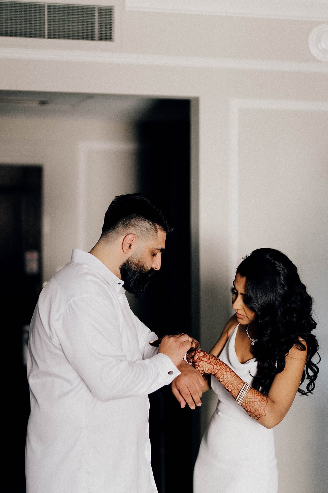A groom helps a bride put on a bracelet.  