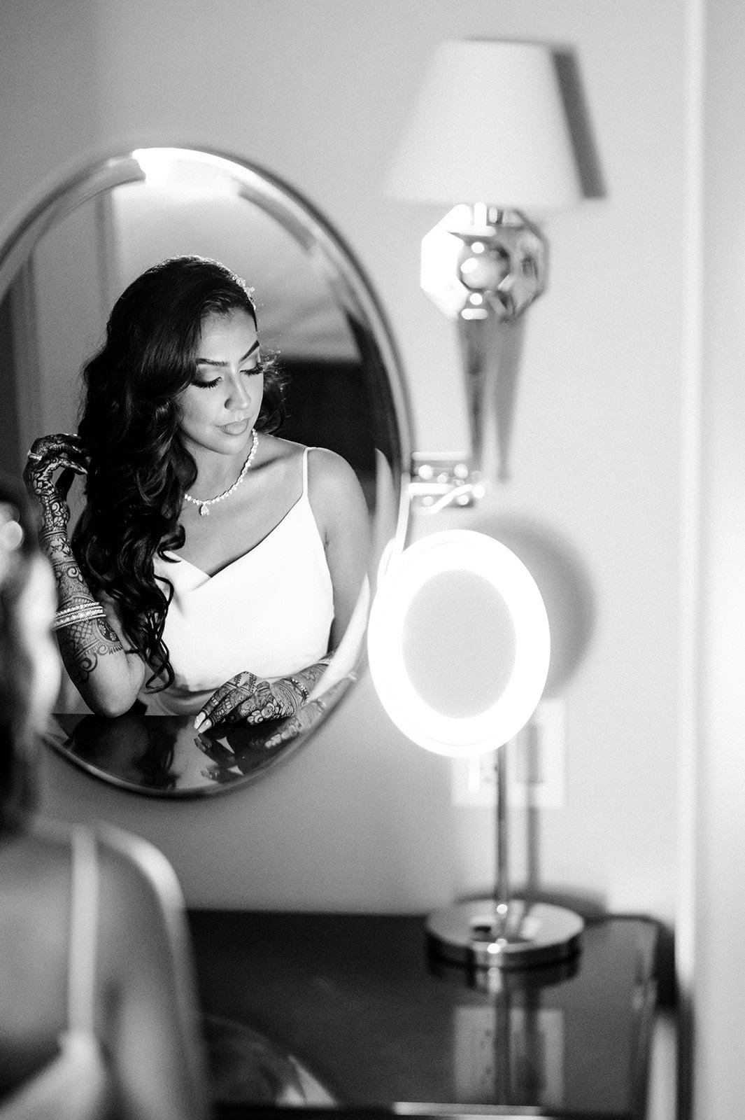 A bride adjusts her hair in a hotel mirror as she prepares for her reception. 