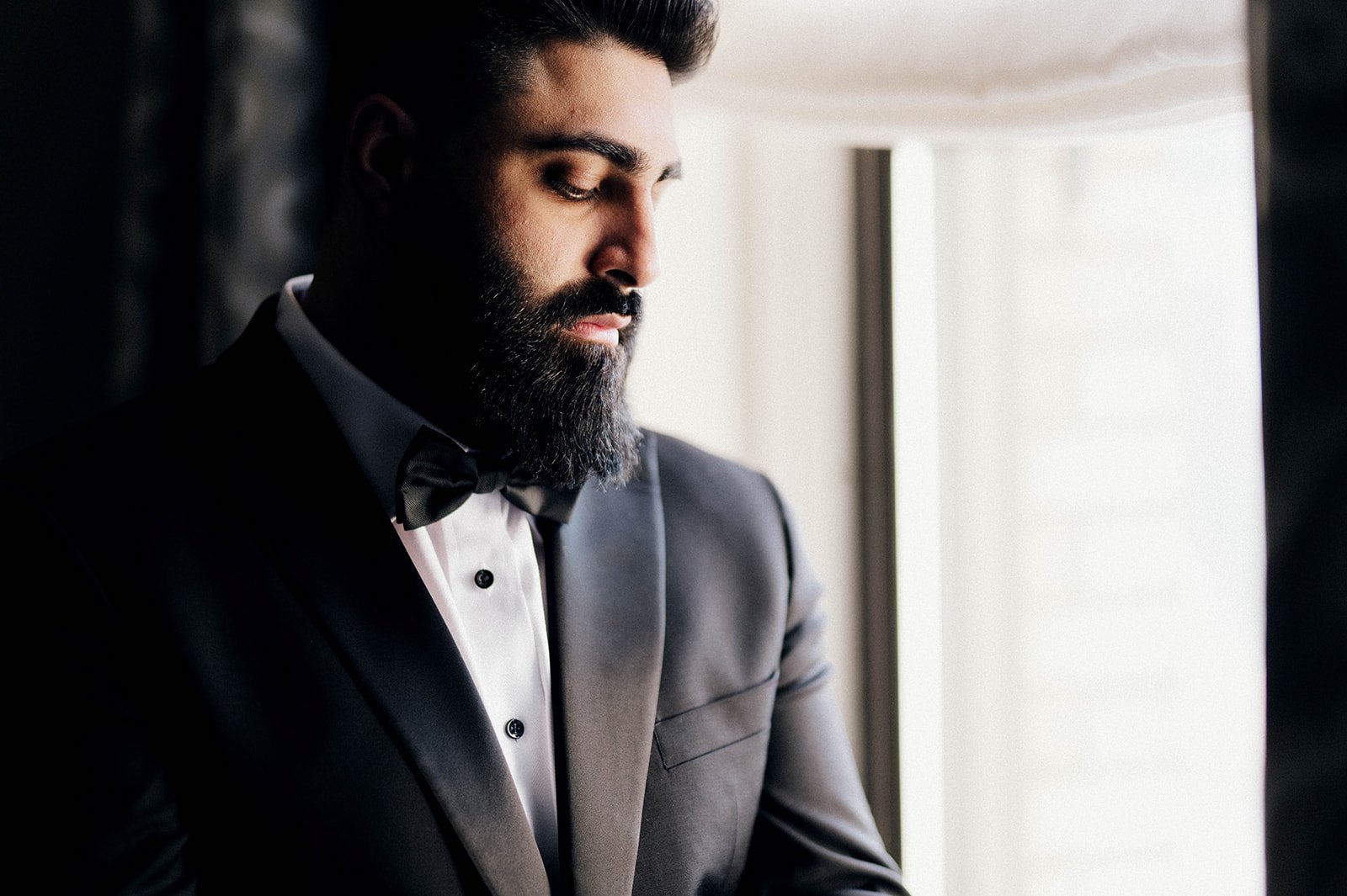 A groom looks out the window as he gets ready for his reception.