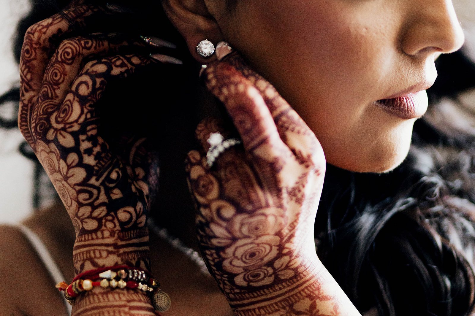 A close up of a brides henna covered hands as she puts in an earring.