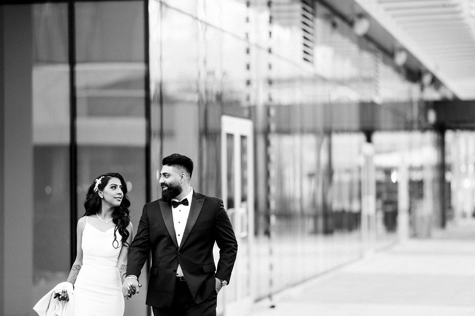 A bride and groom hold hands in front of a glass wall in Vancouver BC.