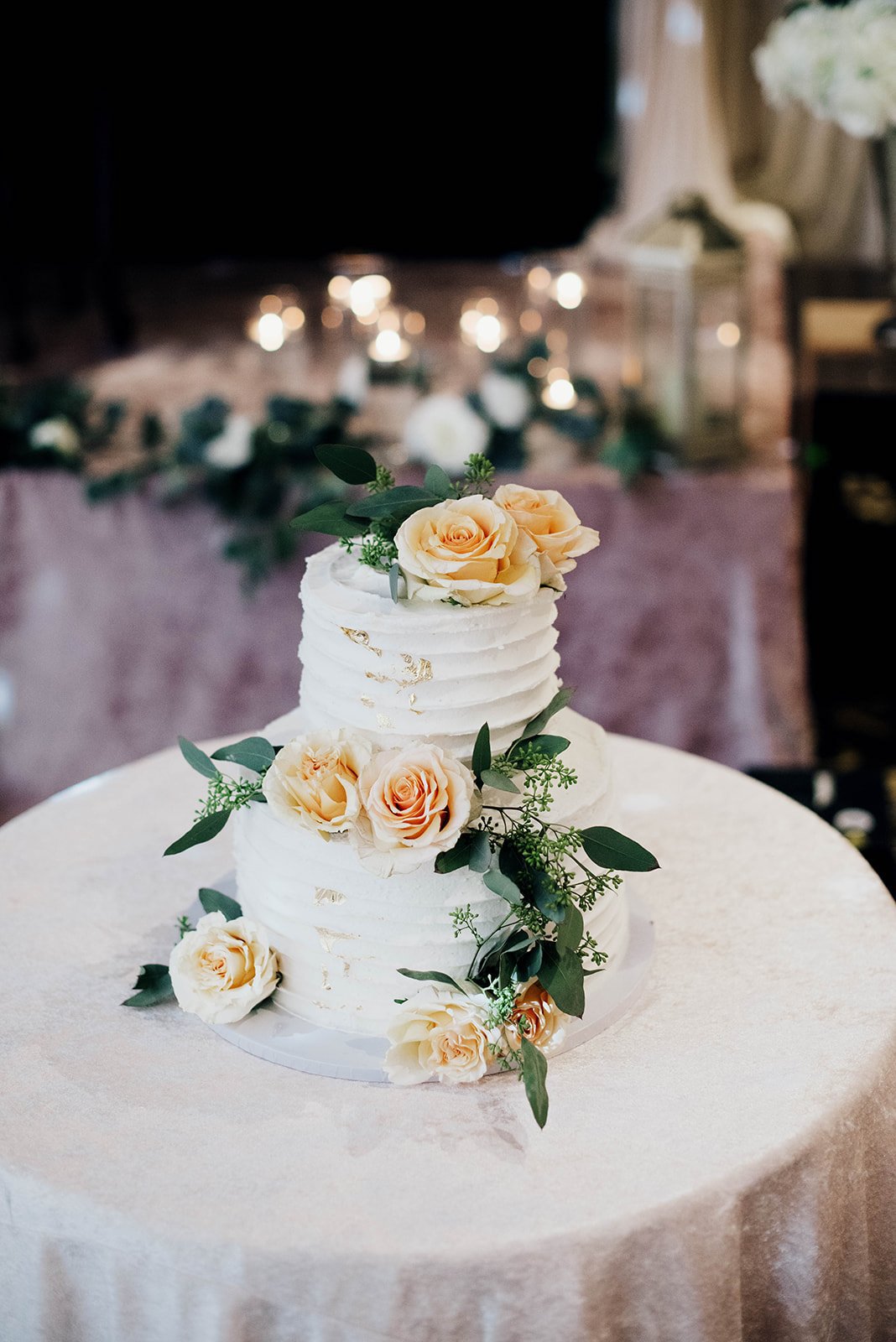 An elegant white frosted wedding cake with yellow flowers and green leaves rests on a table.