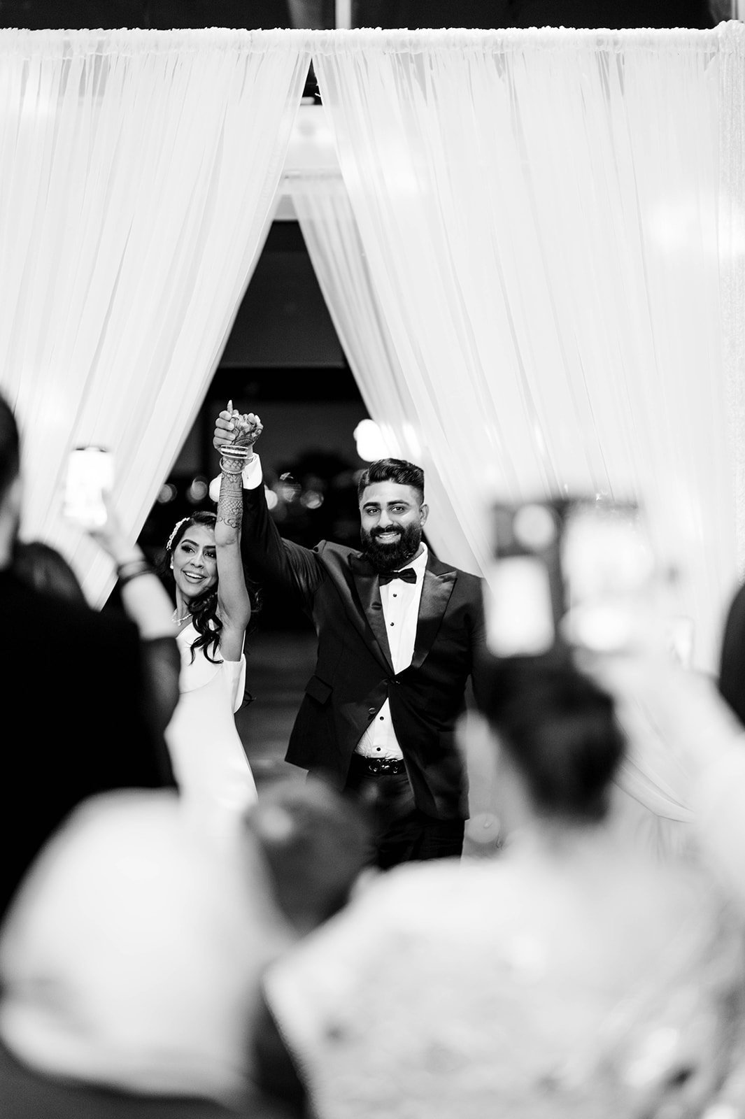 A bride and groom raise their arms triumphantly as they enter their wedding reception.  
