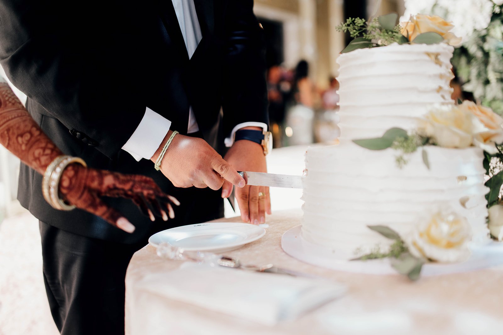 a close up of a groom cutting a wedding cake with his wife's assistance. 