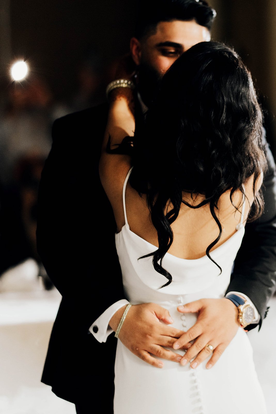 A groom rests his hands on the small of his wife's back during their first dance.