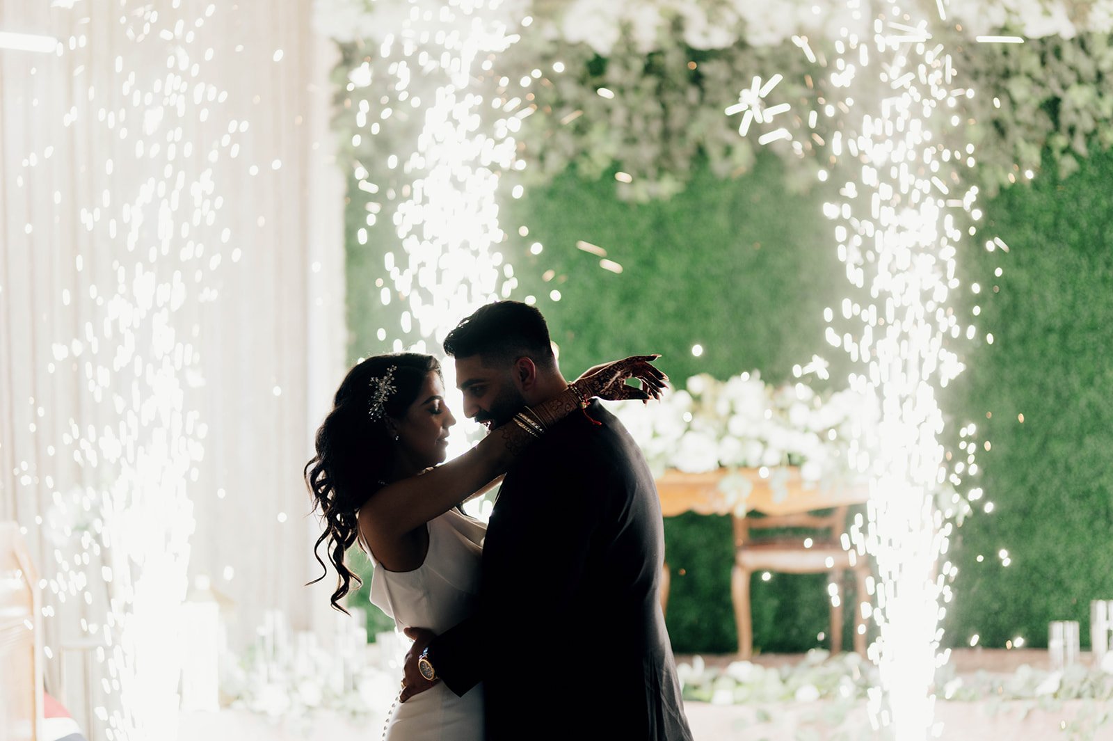 A bride an groom dance in front of sparklers. 