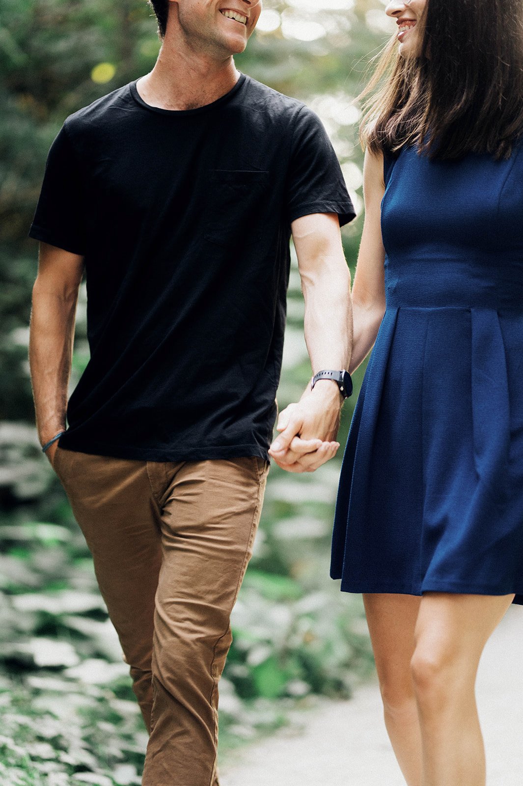 A woman in a blue sundress clutches the hand of her lover as she walks through the woods in Vancouver, BC.