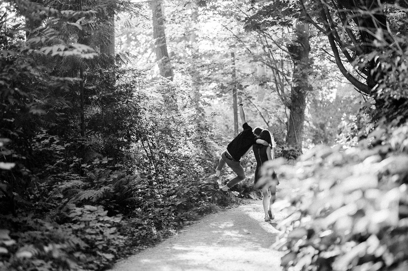 A man leaps for joy, and a woman tolerates his shenanigans as they transverse down a wooden path in Vancouver BC. 