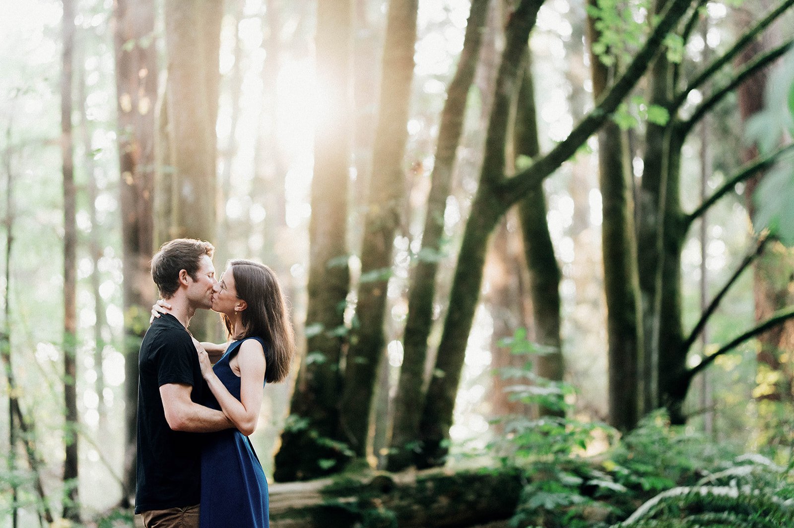 A woman kisses her fiancee as they enjoy a quiet moment in the woods during sunset in Stanley Park.