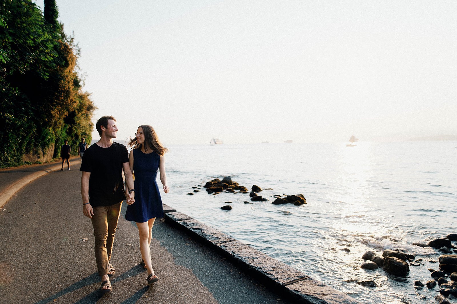 A nerdy couple stroll on the seawall at English Bay on a clear sunny day in Vancouver BC.