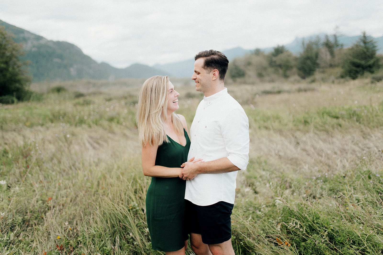 A couple laugh as they hold each other in a grassy field in Squamish, BC.