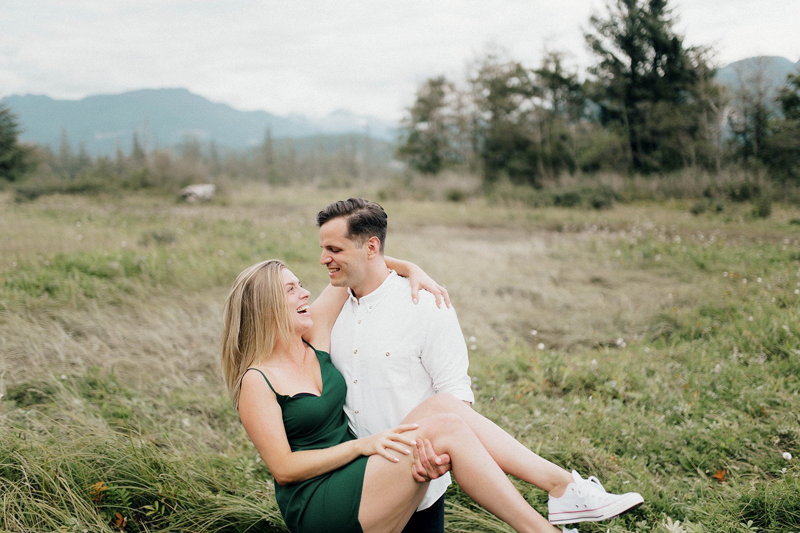 A man twirls around his fiancee in a grassy field in Squamish, BC.