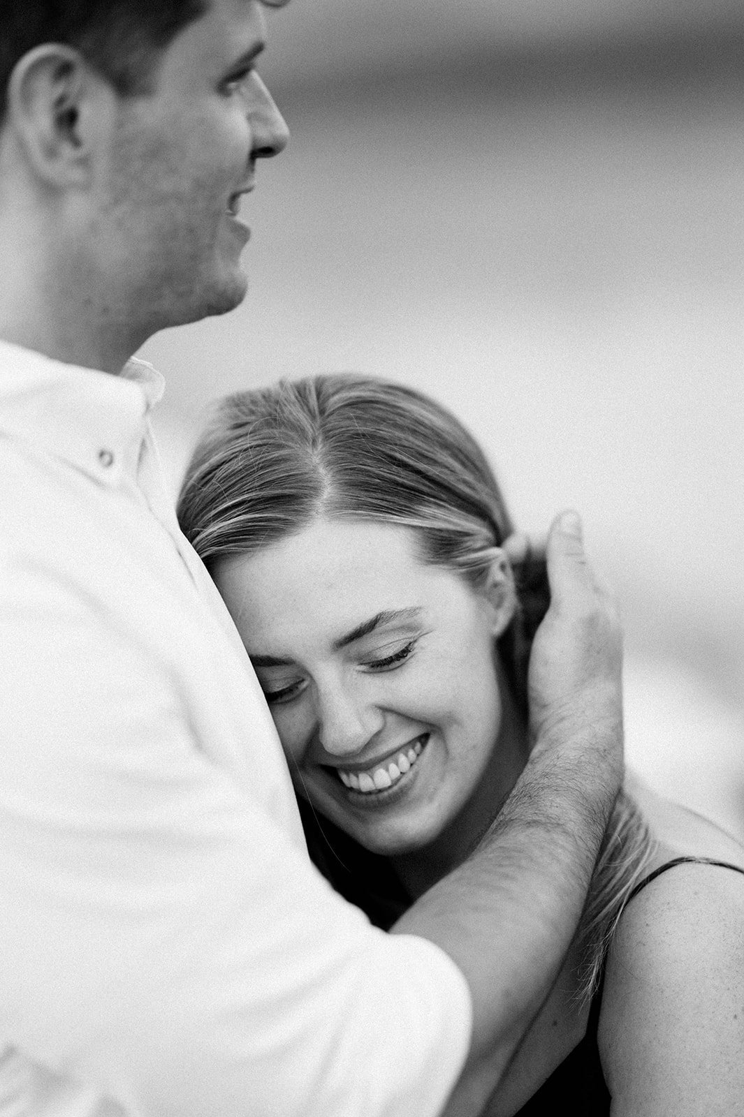 A bride to be rests her head on her fiancée's chest as he runs his fingers through her hair in a peaceful moment on the beach.