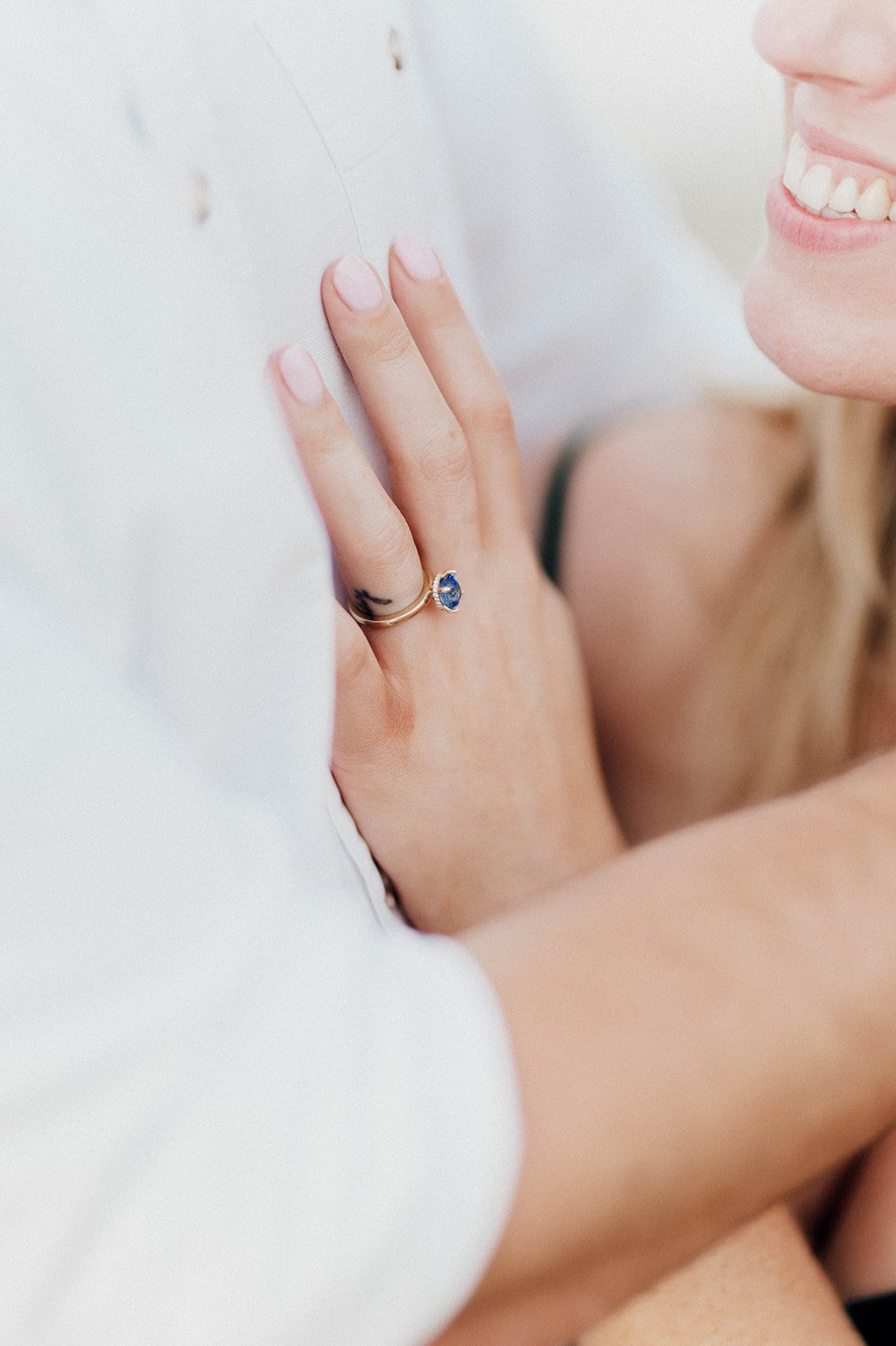 A sapphire ring shines on a brides hand as she smiles at her groom.