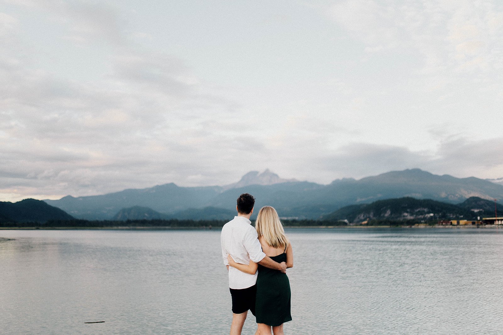 A man and woman look out  at the lake in front of them, surrounded by mountains in Squamish, BC   