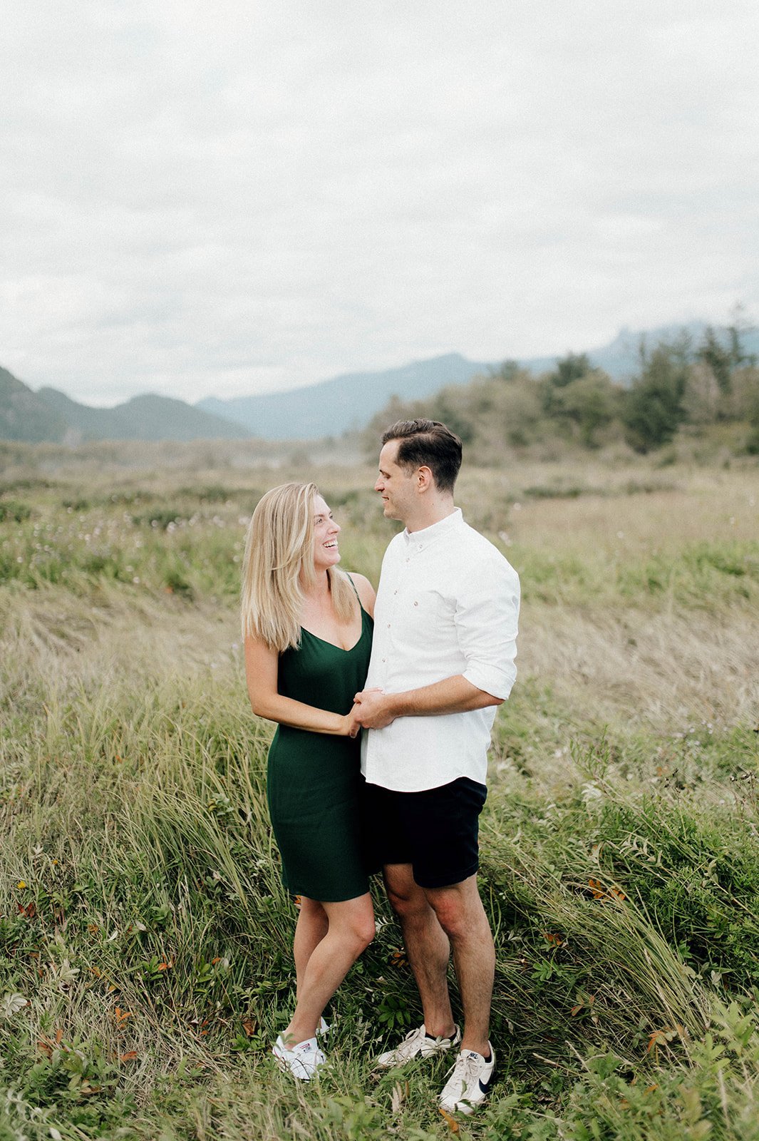 An engaged couple look at each other lovingly as they stand next to one another in a lush field. 