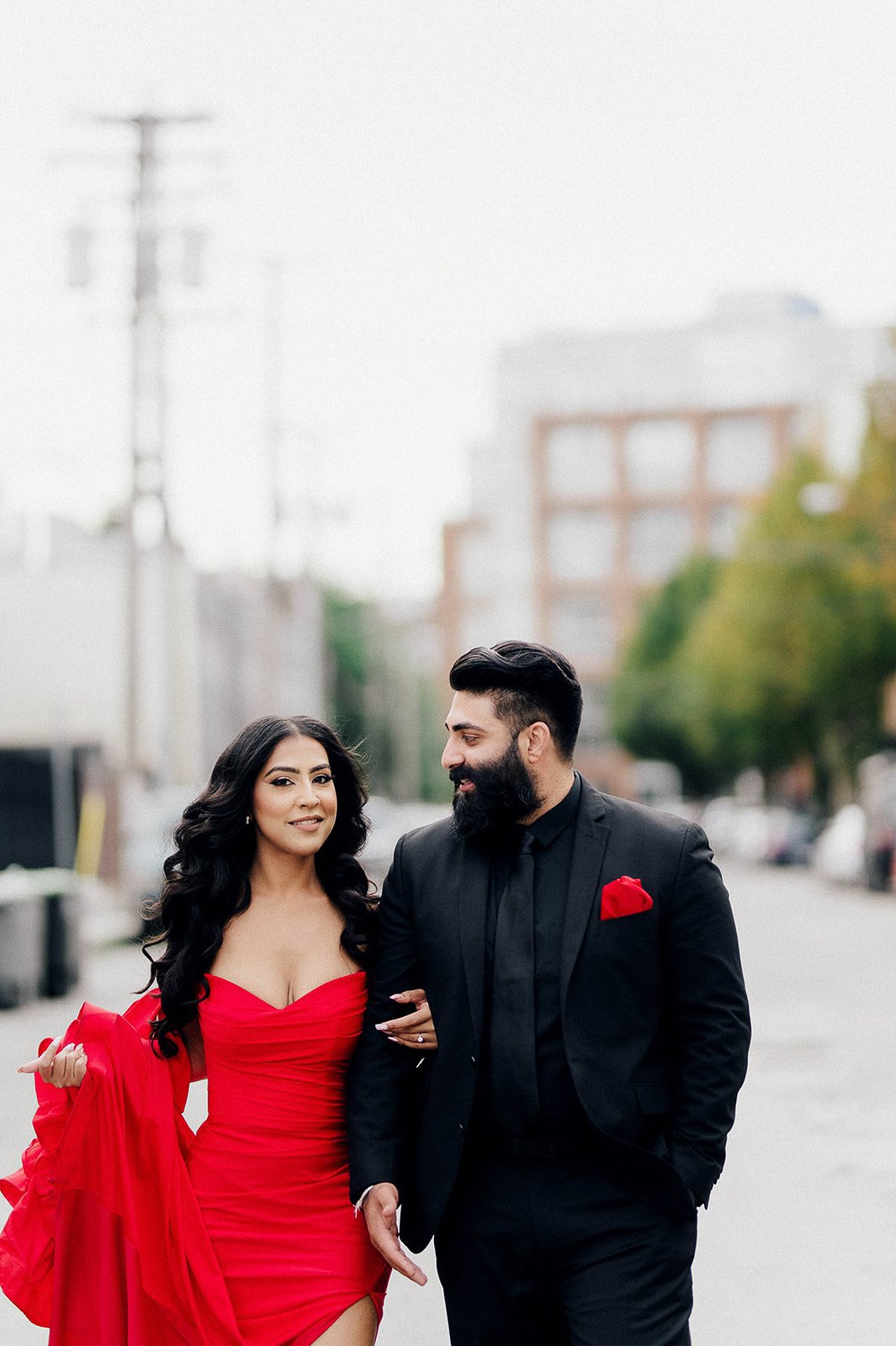 a woman wearing a chic red gown and man wearing a black suit during their engagement session in Vancouver, BC.