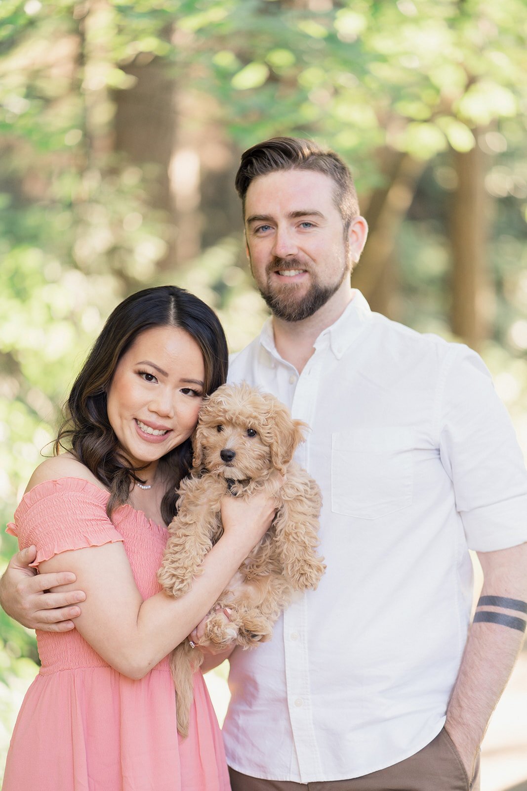 A hip looking engaged couple poses for the camera with their adorable curly-hair golden-doodle puppy.