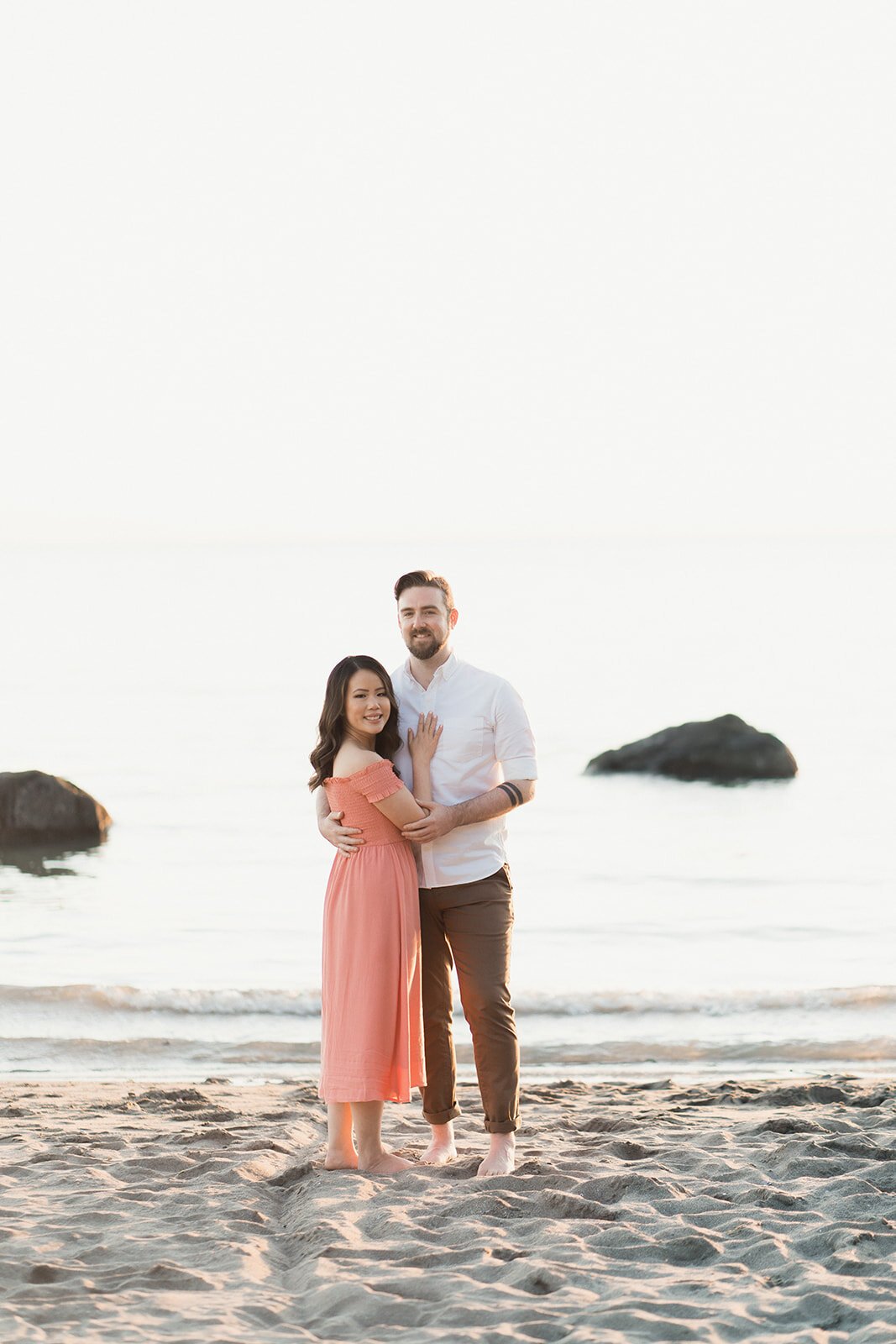 An engaged couple stand on a soft sandy beach lit by a gorgeous sunset.