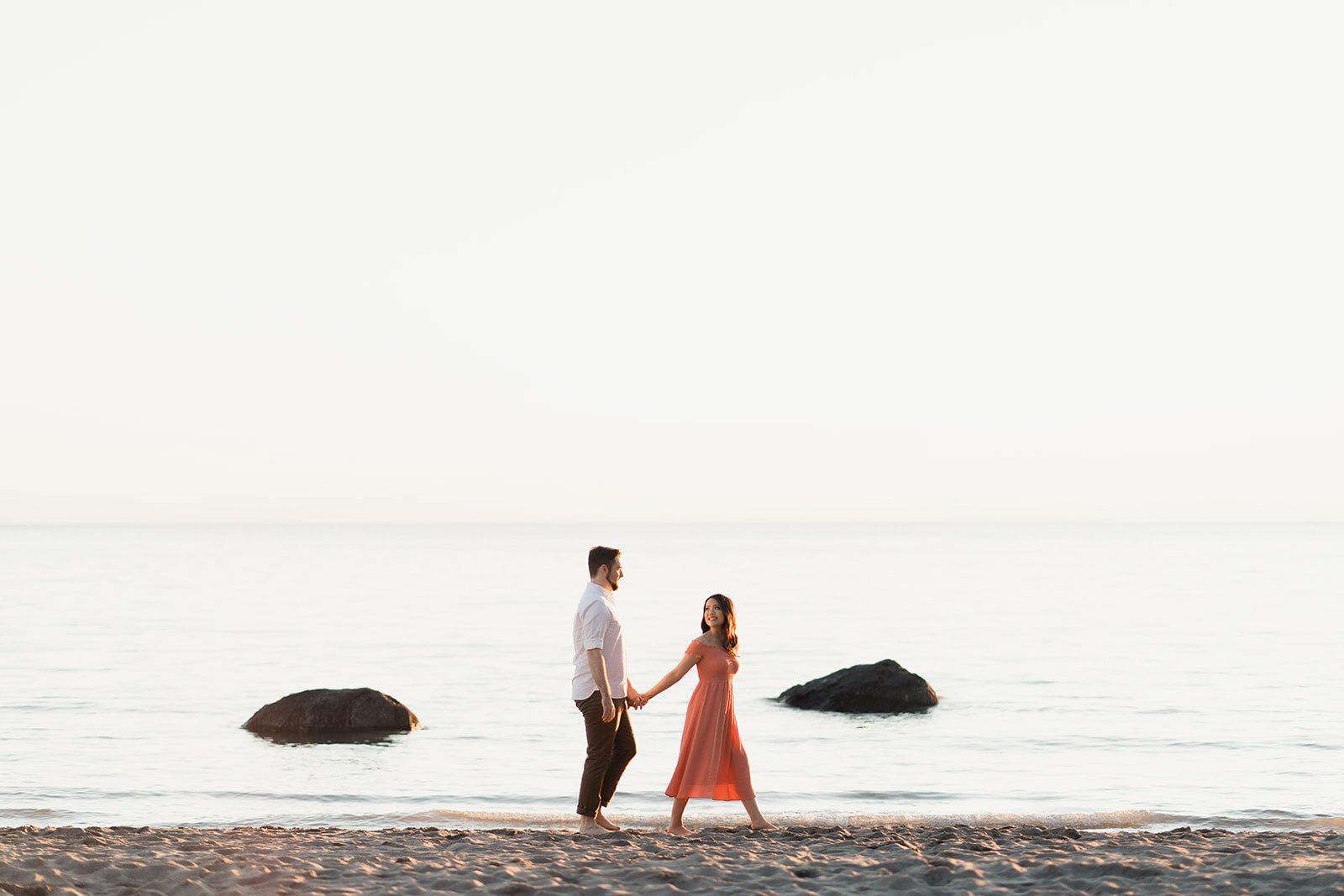 An engaged couple walk on a beach at English Bay during sunset.