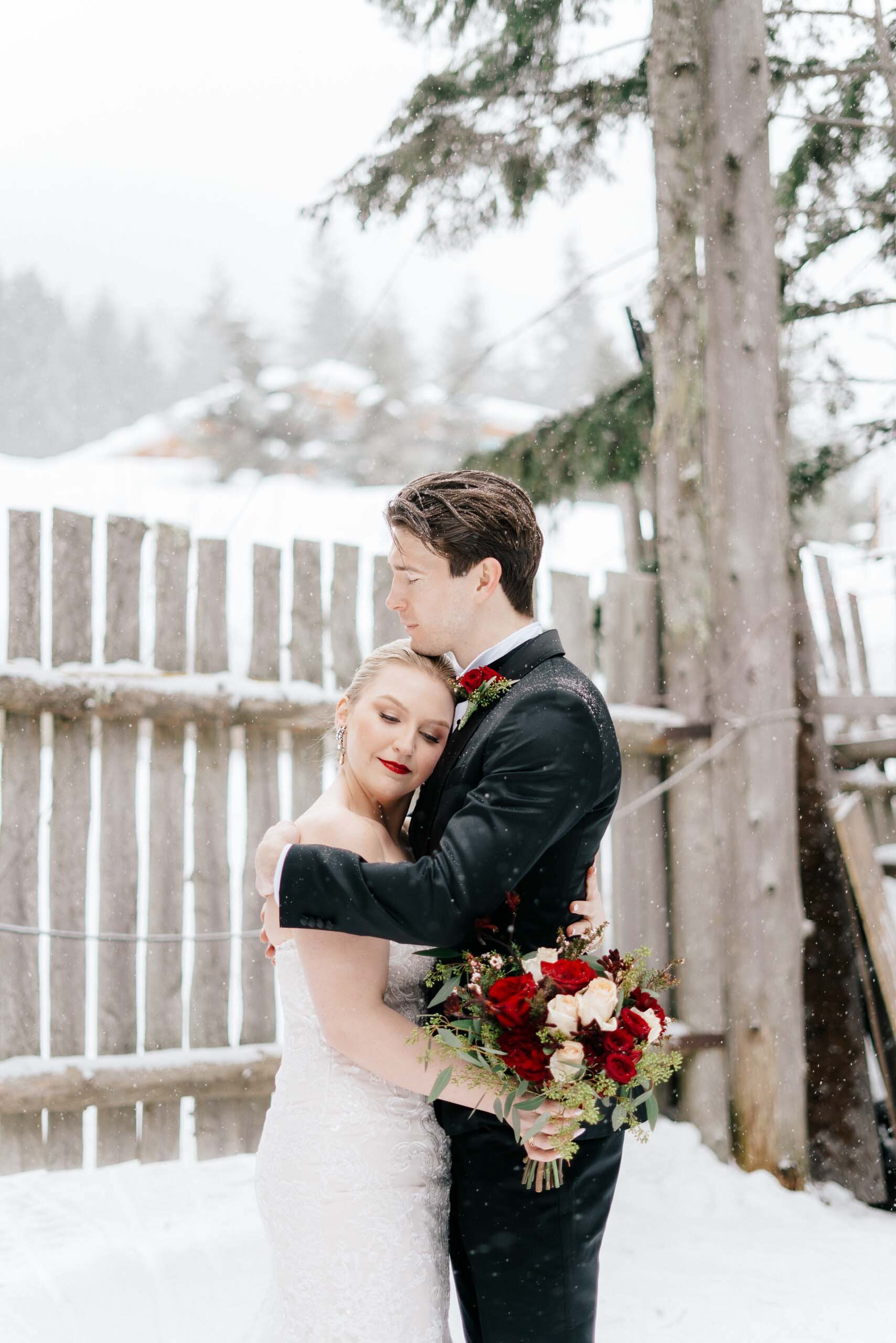 A groom pulls his bride into a warm hug on a cold snowy day in Whistler, BC. 