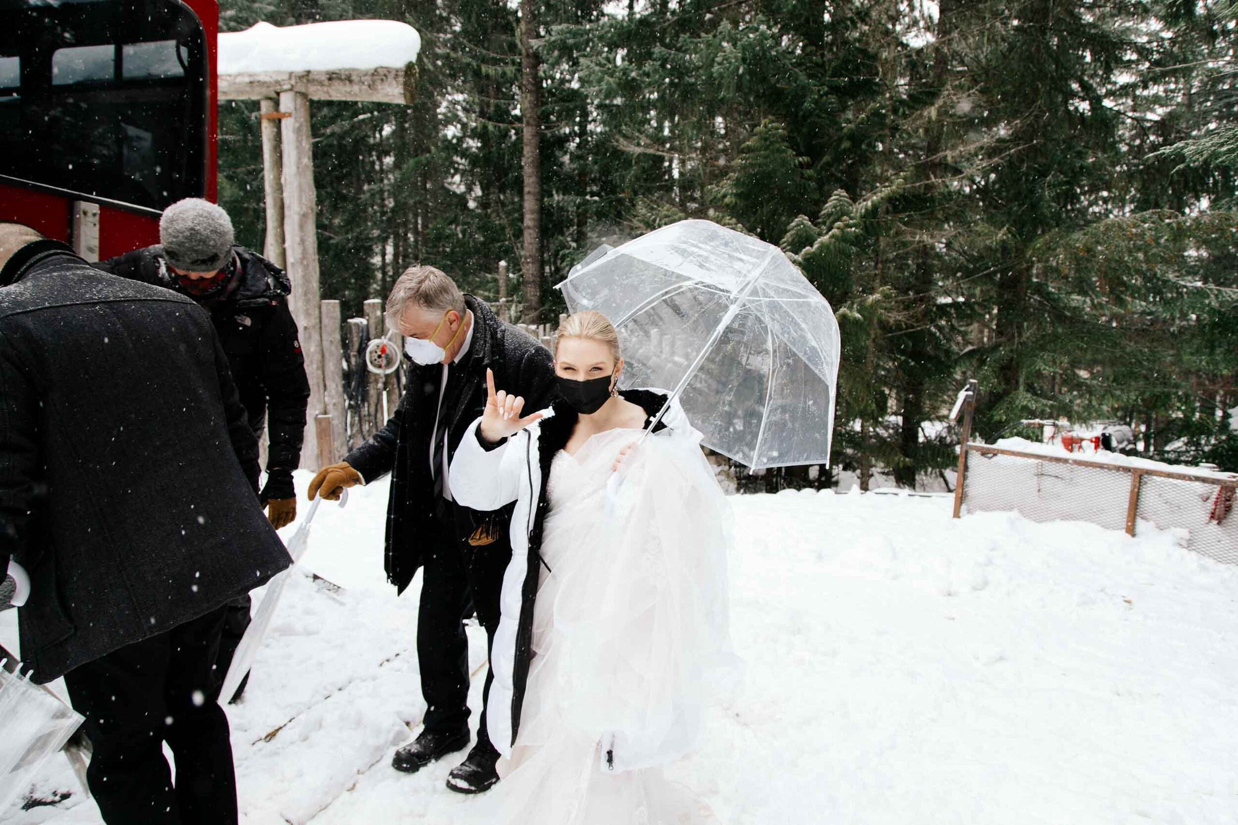 A bride wearing a black mask flashes a gang sign to the camera as she boards a snowmobile. 