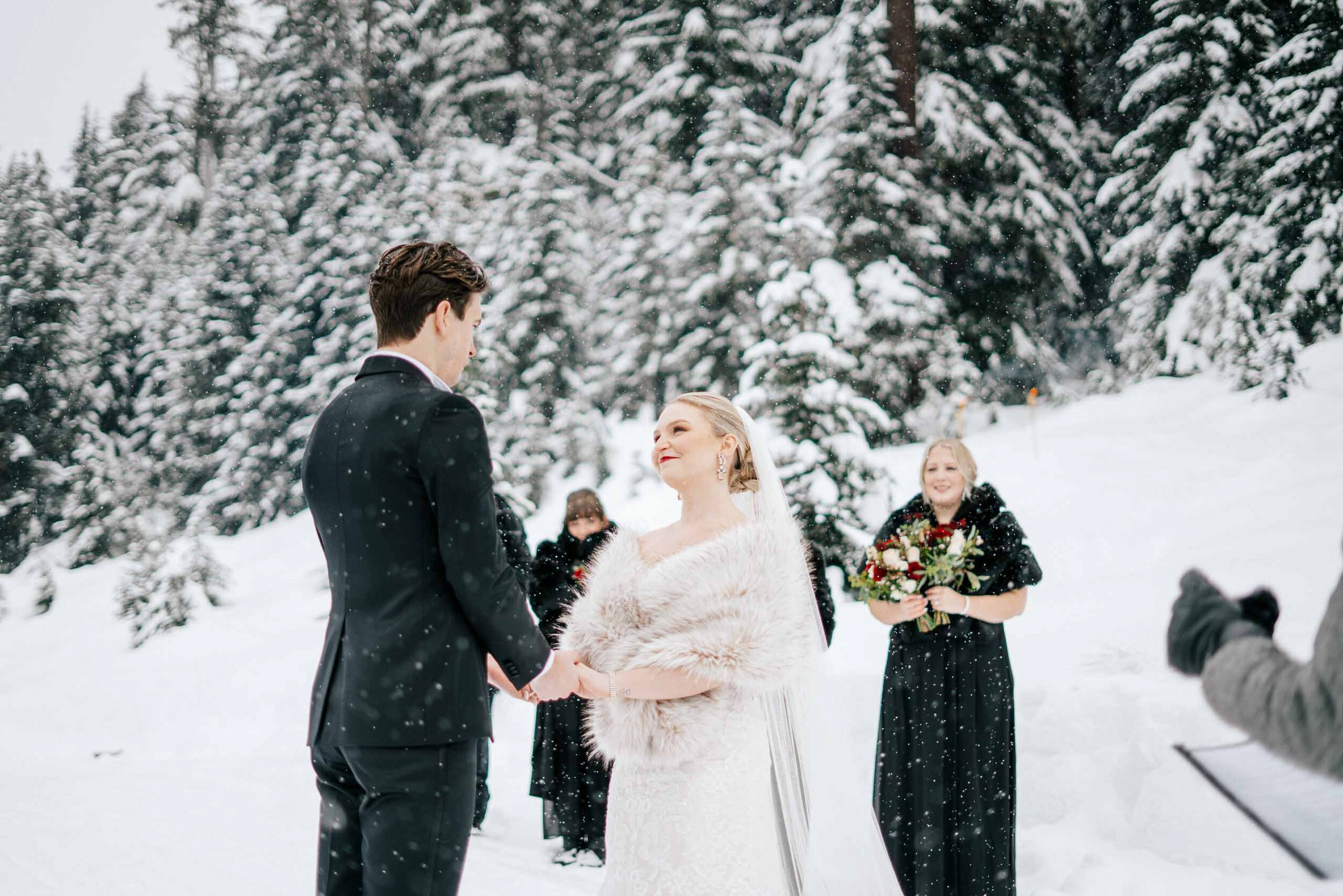 A bride and groom hold hands during their ceremony as the snow falls in Whistler BC