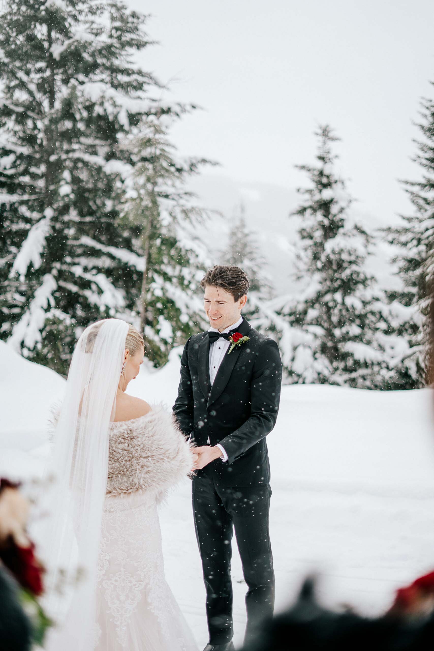 A bride and groom hold hands and smile during their ceremony as the snow falls in Whistler BC