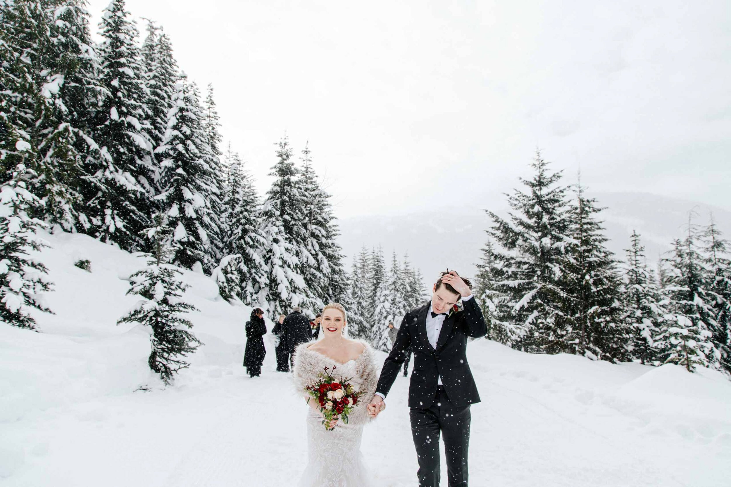 A bride and groom hold hands as they walk through the falling snow during their outdoor wedding. 