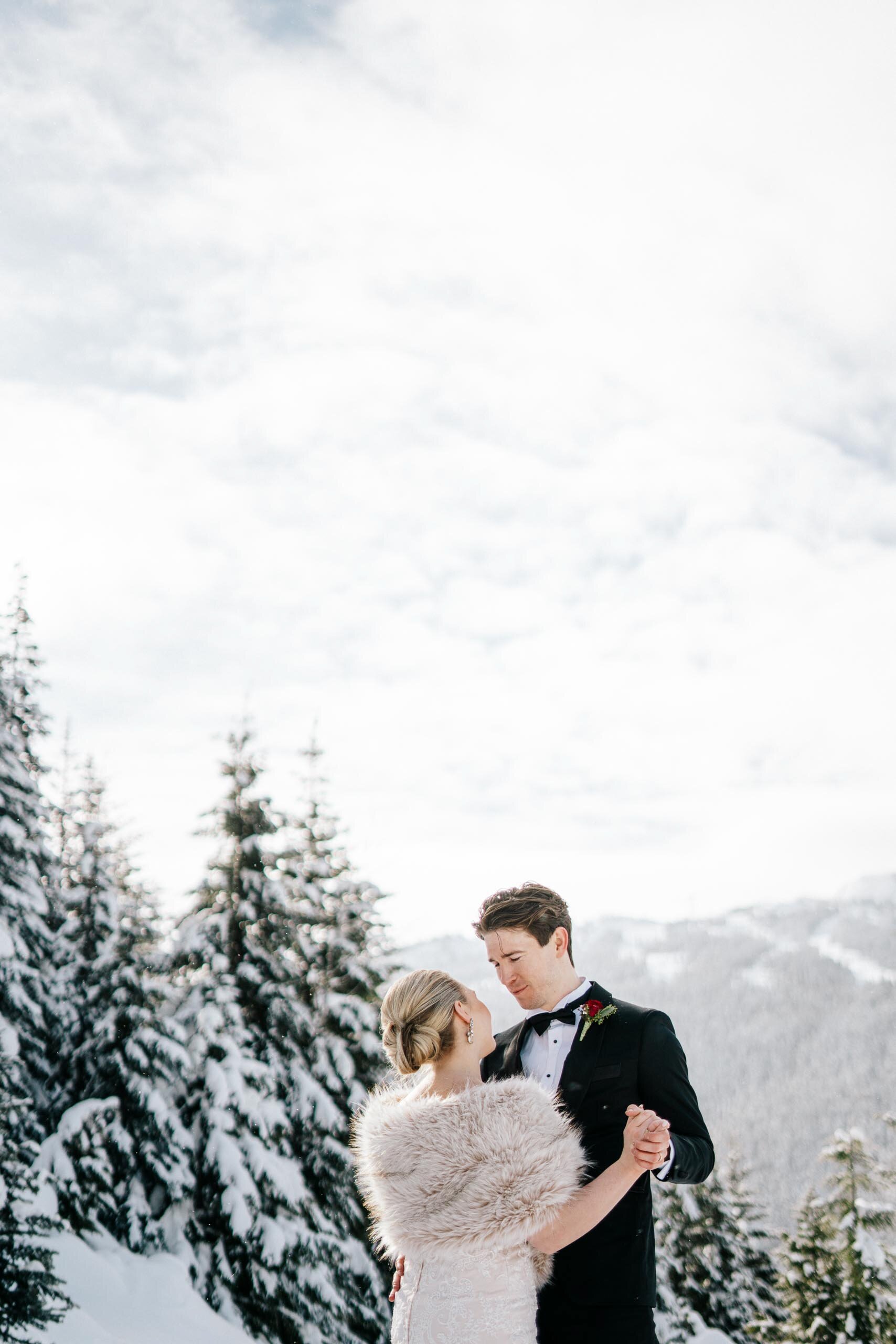 A bride in a fur stole holds her groom surrounded by snowy evergreens at their Whistler BC Weddin