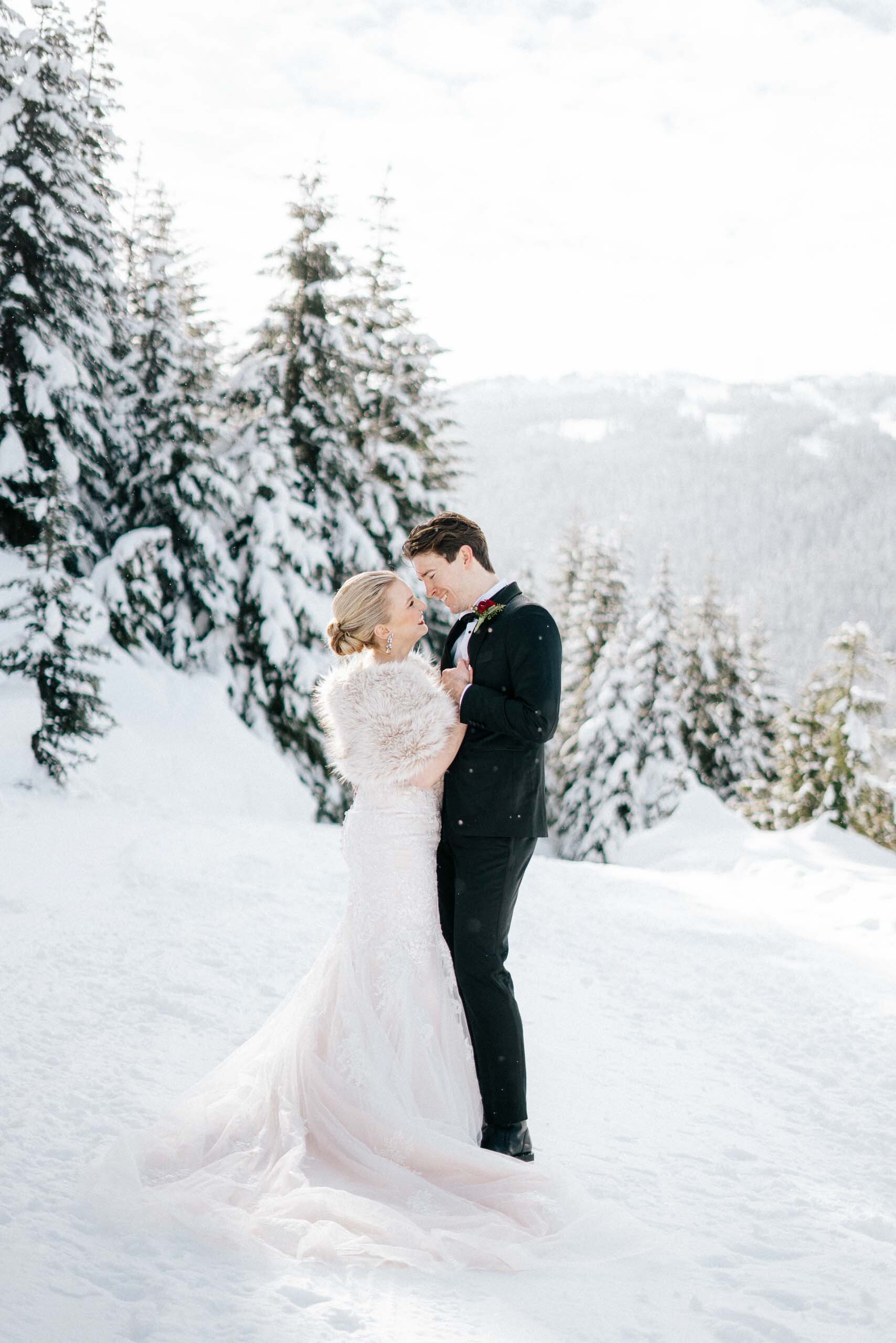 A bride in a fur stole holds her groom surrounded by snowy evergreens at their Whistler BC Weddin
