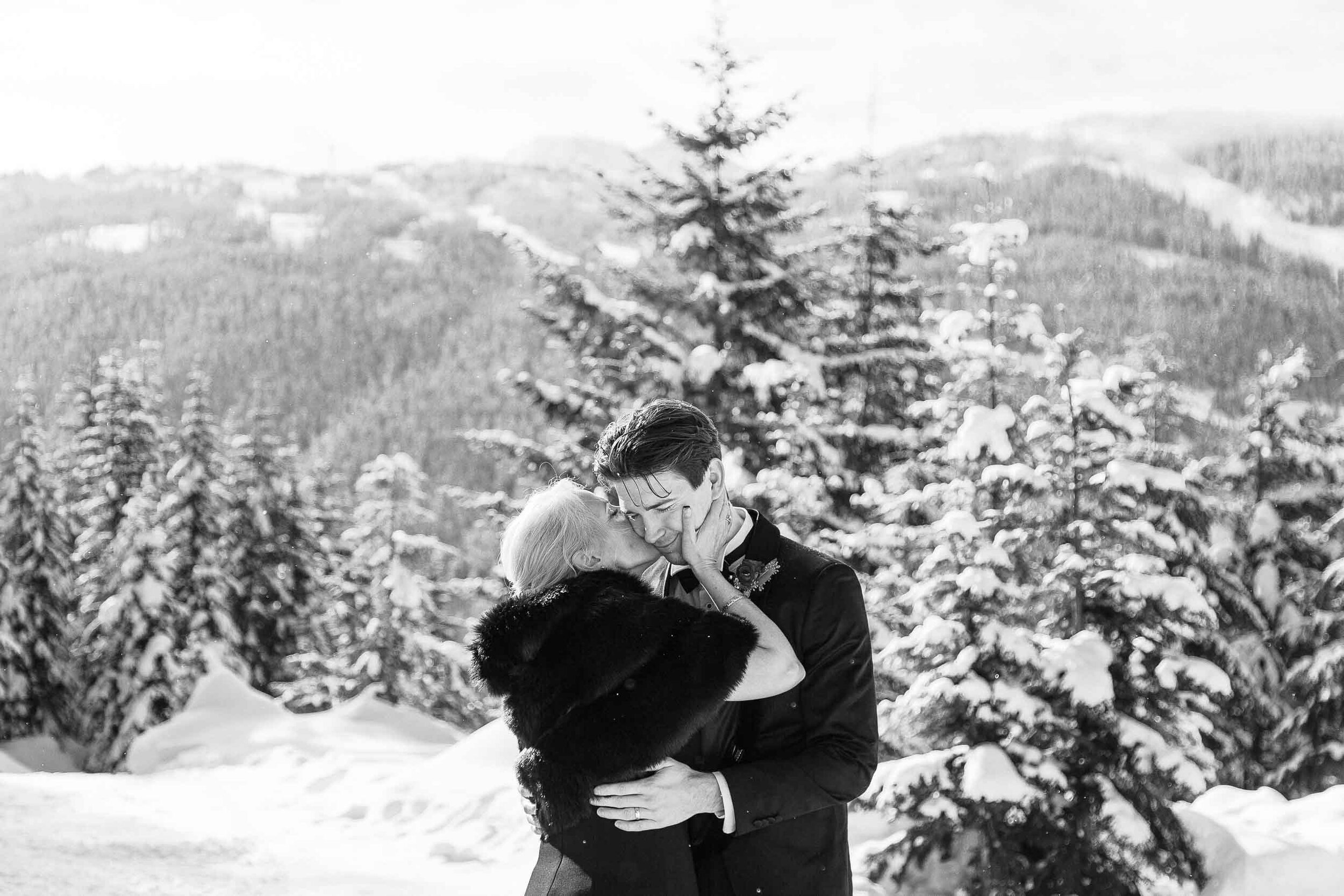 The mother of the groom kisses her son on the cheek during his outdoor winter wedding. 