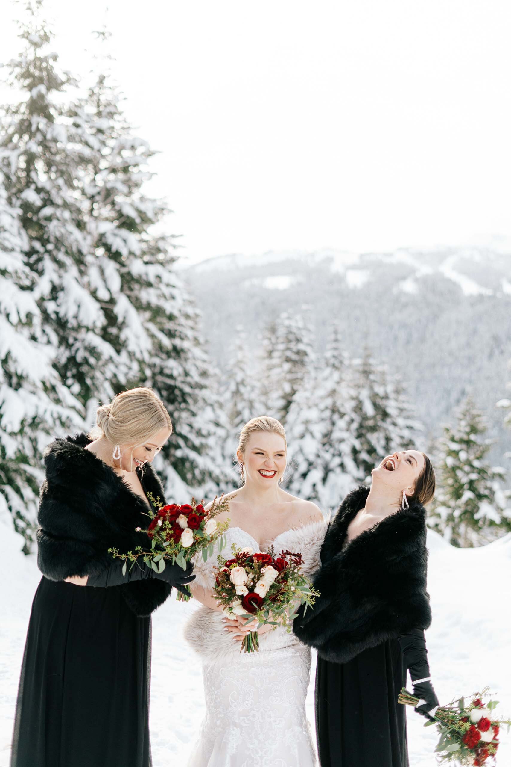 Bridesmaids in matching black fur stoles laugh with the bride as they enjoy the cool outdoor weather. 