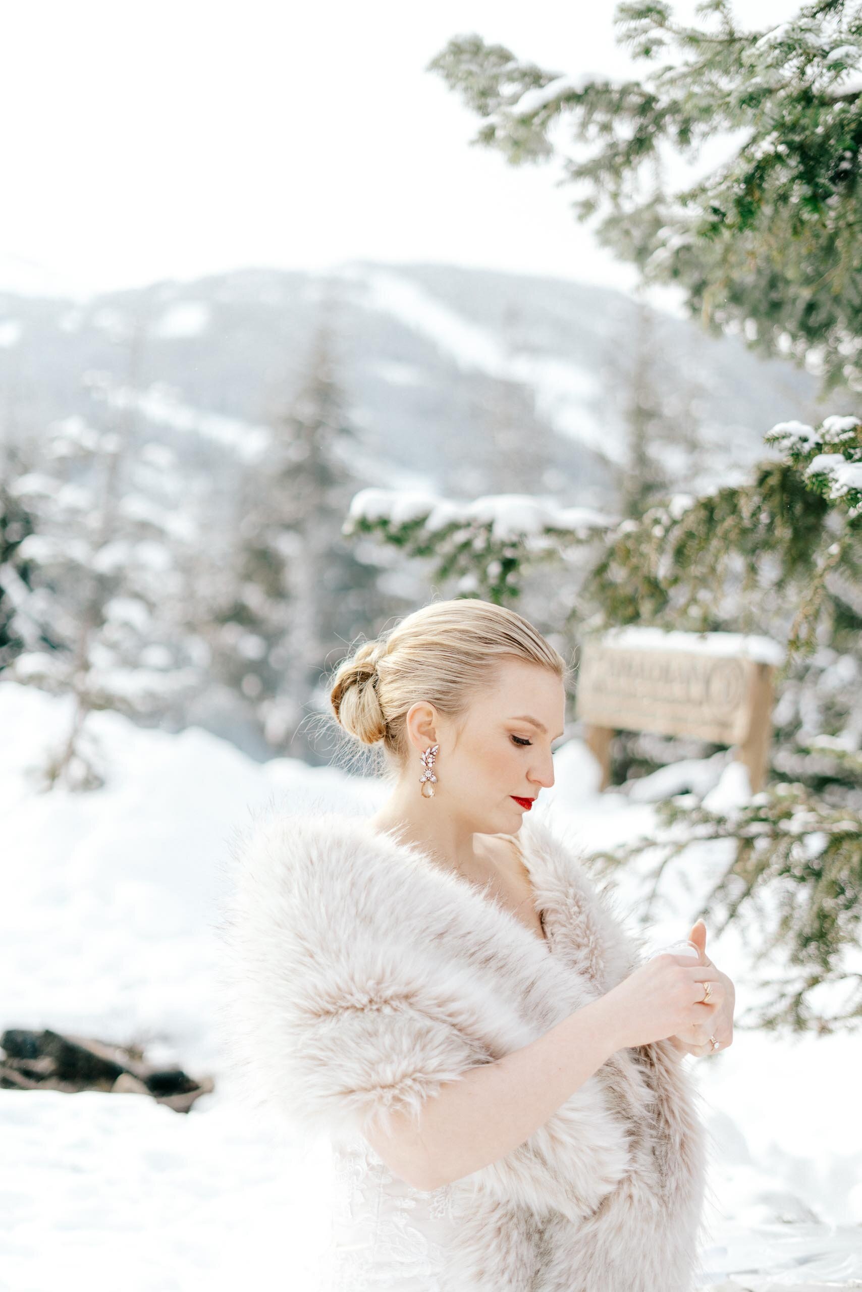 A pale blonde in a fur stole considers her wedding ring as she stands in the snow.