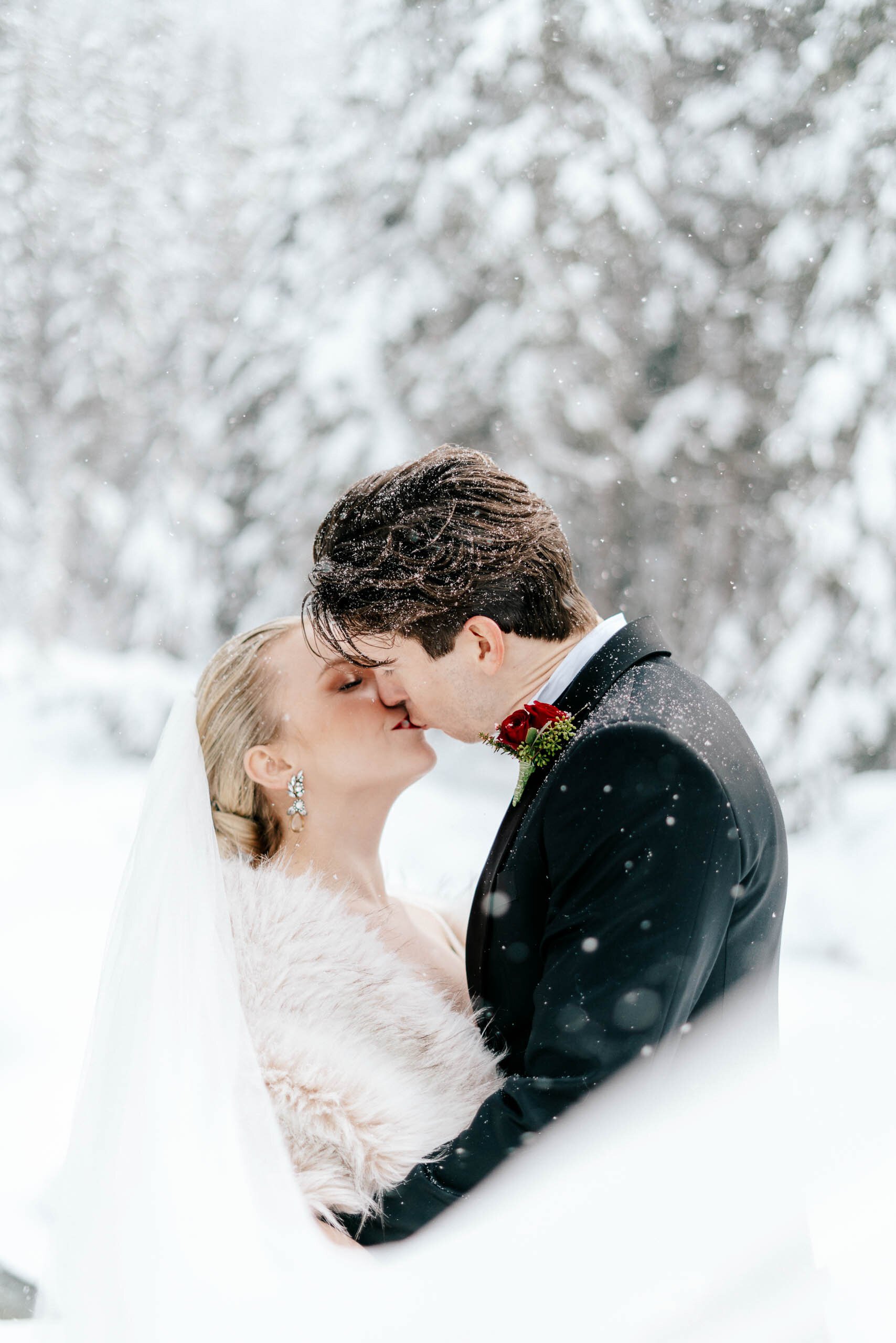 A beautiful bride and groom kiss in the snow as the snow falls around them in Whistler BC.
