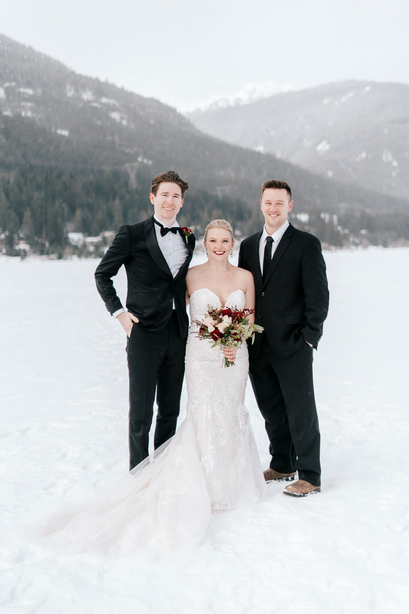 A groomsman smiles as he poses next to a bride and groom in the snowy mountains of Whistler, BC.